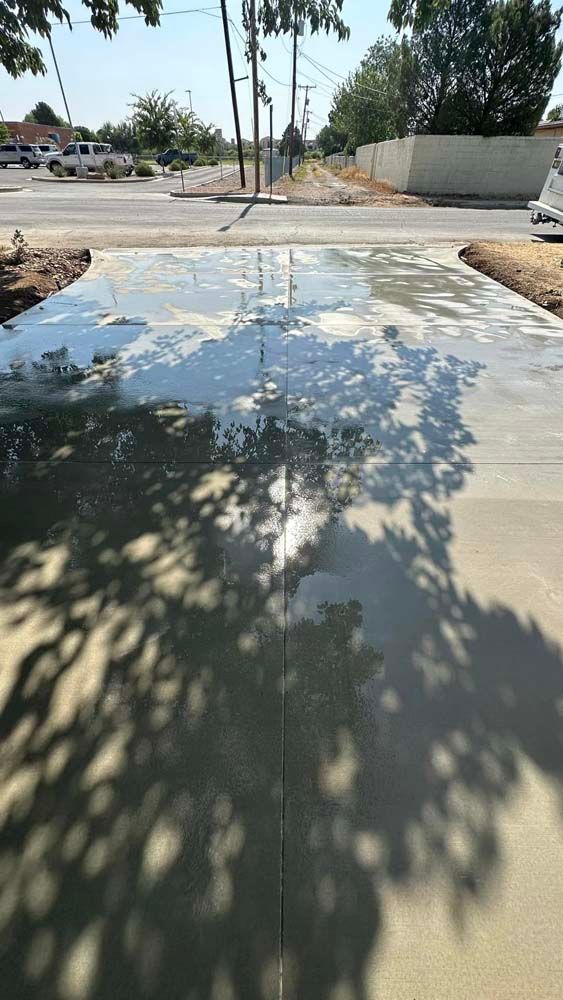 A puddle of water on a sidewalk next to a road with trees in the background.