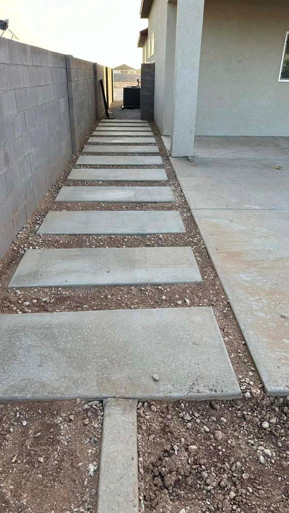 A concrete walkway leading to a house with a brick wall.