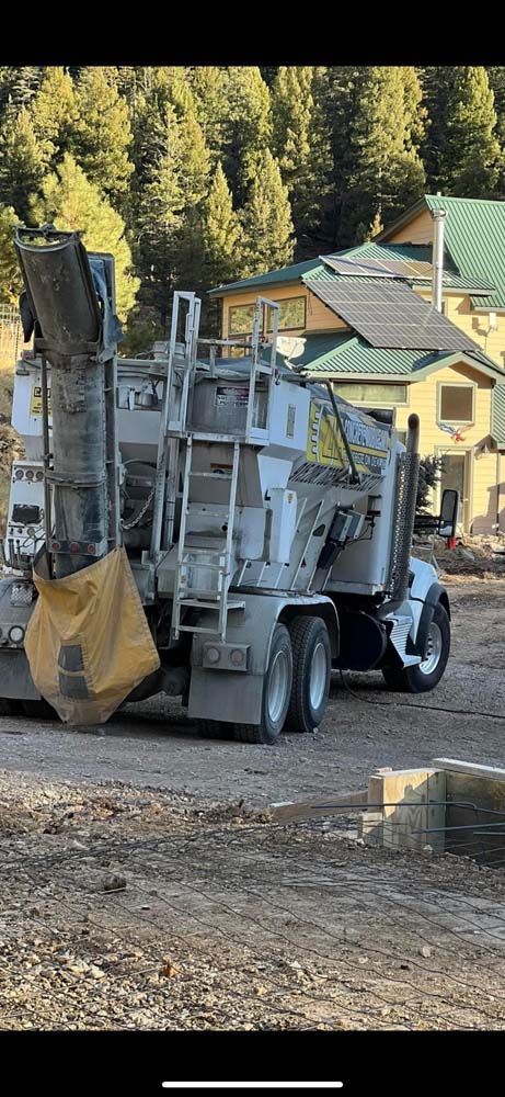 A cement truck is parked in a dirt lot in front of a house.