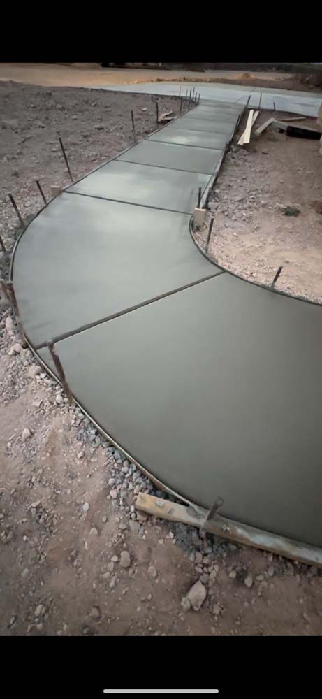 A curved concrete walkway is being built in the dirt.
