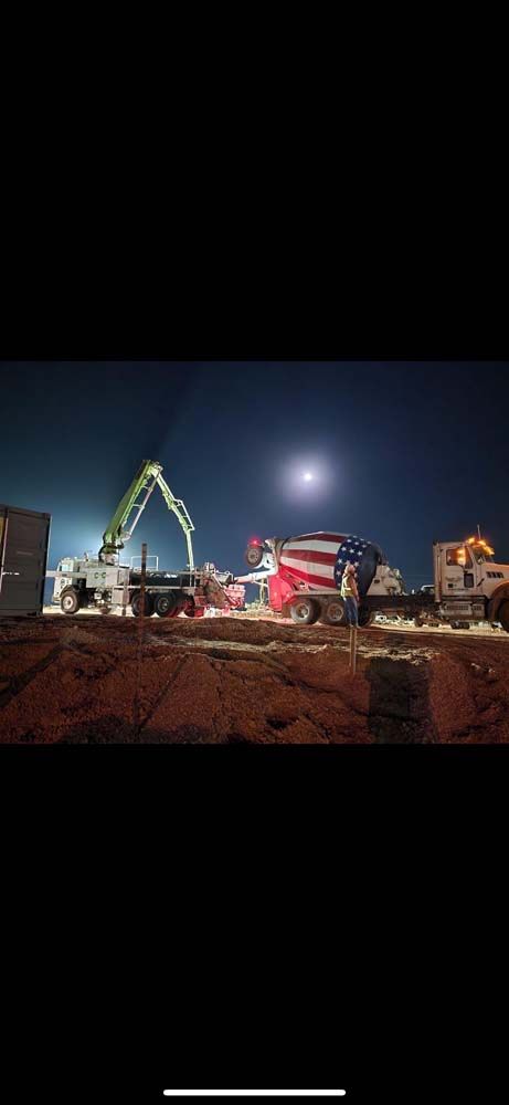 A concrete mixer truck is driving down a construction site at night.