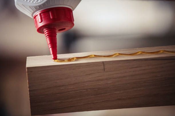 Applying wood glue to a wooden plank with a red-tipped bottle.