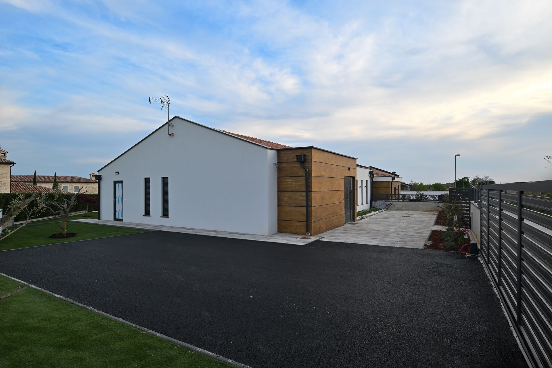 Modern white and brick building with dark asphalt driveway and cloudy sky.