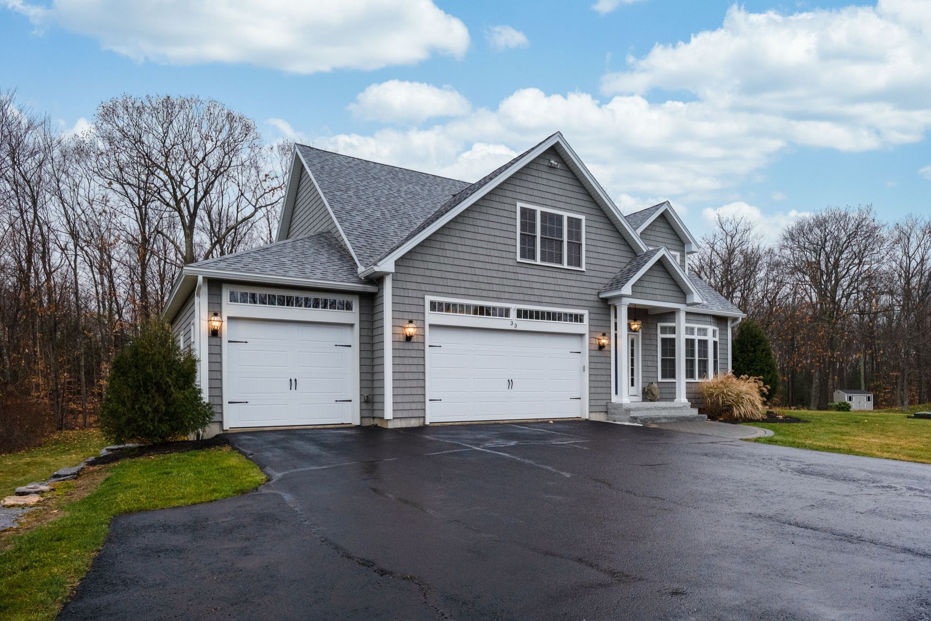A modern gray house with white garage doors, an asphalt-paved driveway, and a landscaped front yard