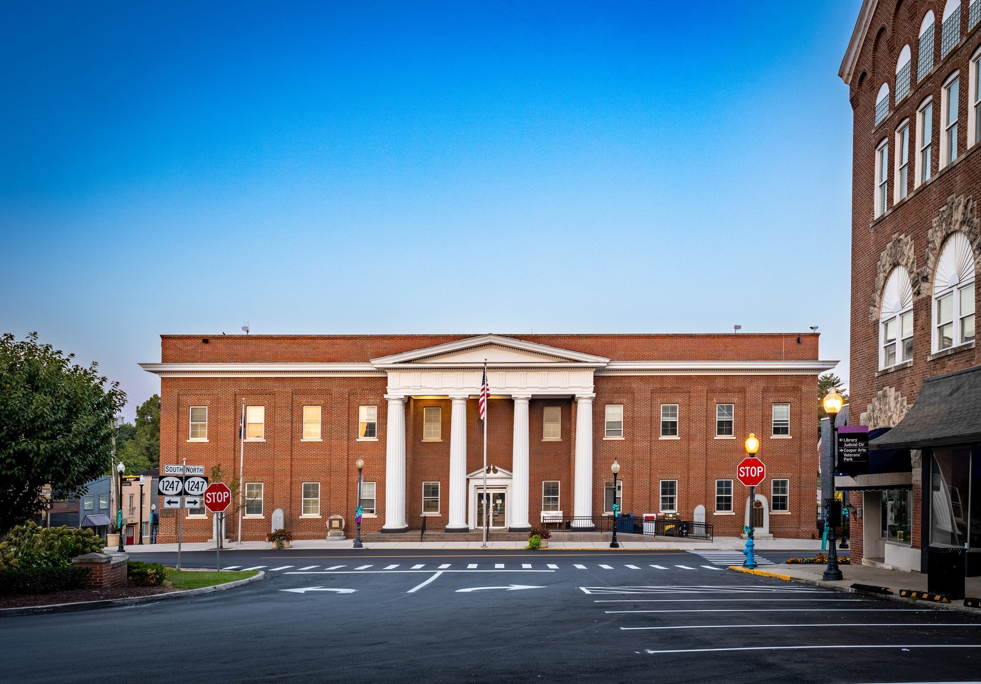 Brick building with white columns, flag in front, street with crosswalk and stop signs.