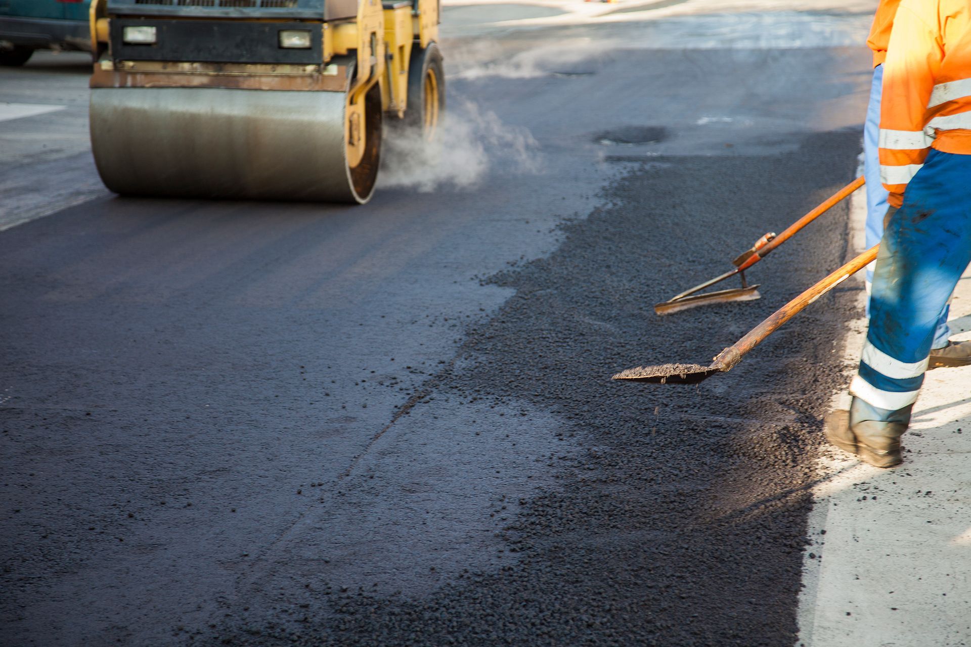 Road paving with a roller, worker, and tools.