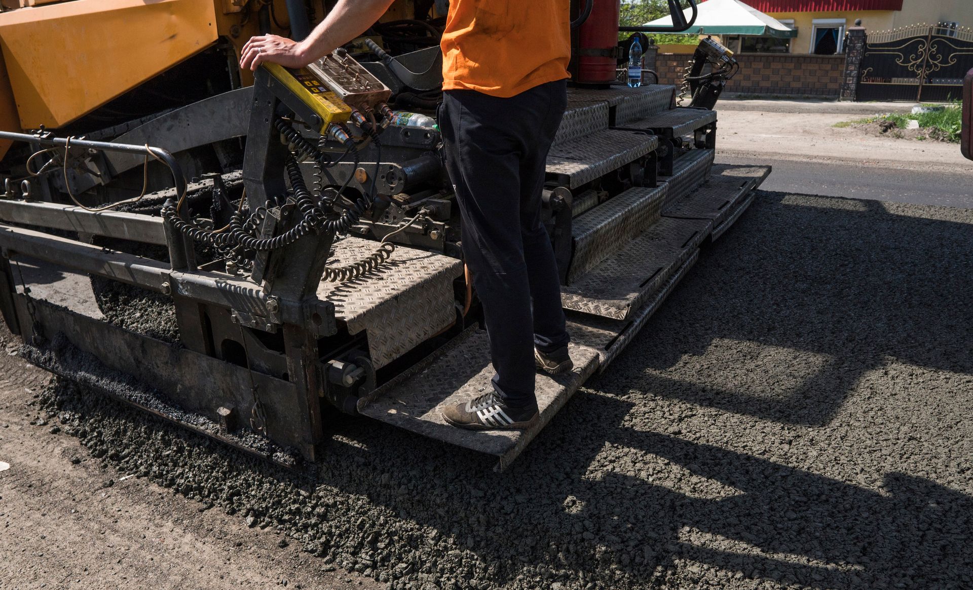Person in orange shirt operating asphalt paving machine on road.
