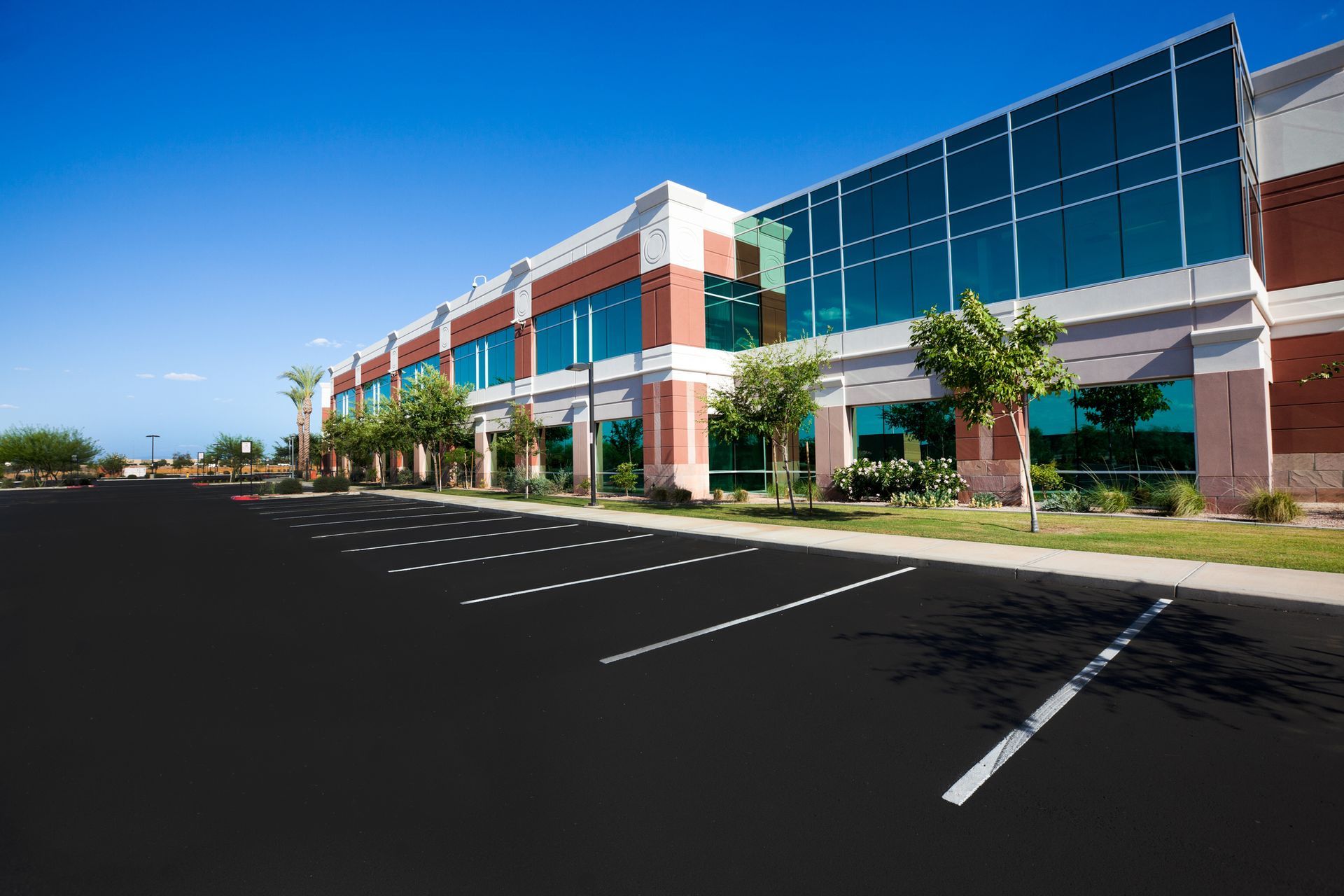 Office building with large windows, red brick, and empty parking lot on a sunny day.