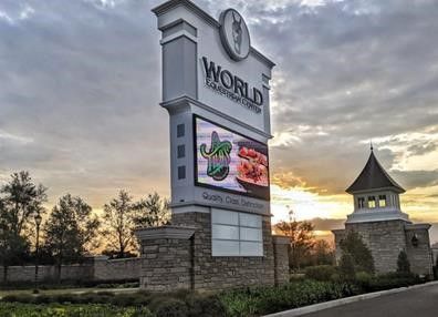 Tall sign for the World Equestrian Center, featuring a digital display, stone base, and a gazebo, at sunset.