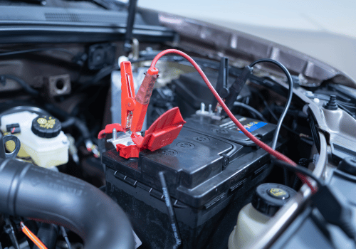 Vehicle battery with red jumper cable clamps attached inside the engine bay for battery service