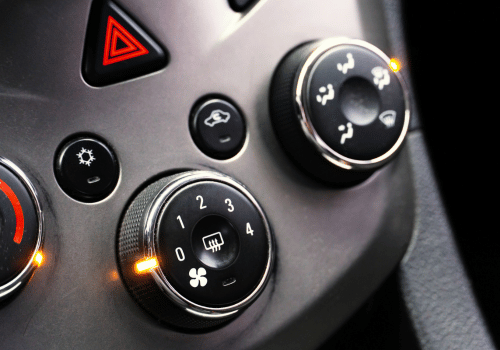 Close-up of car dashboard climate controls and hazard button with illuminated indicators.