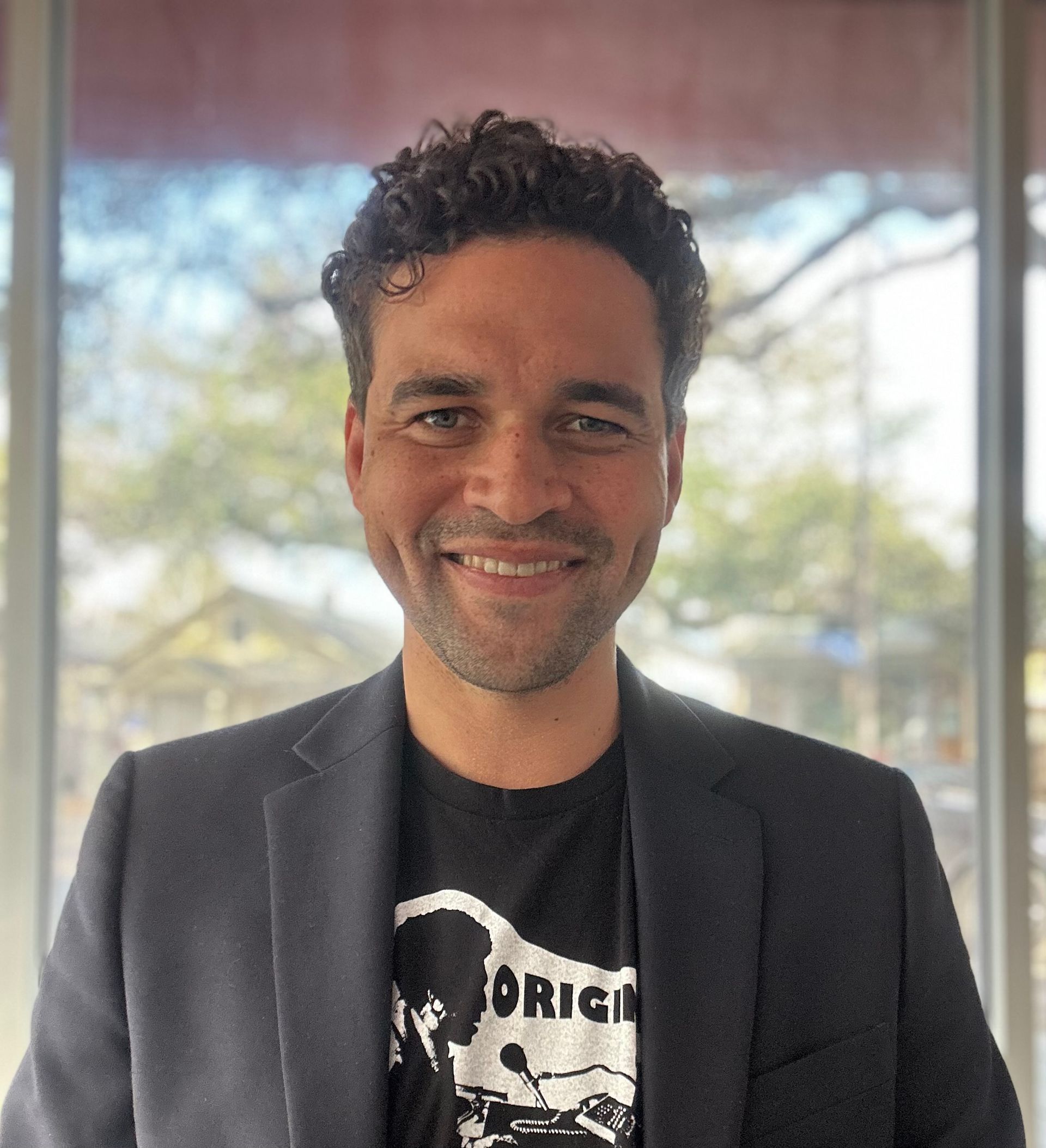 A man in a suit and a black shirt is smiling for the camera.