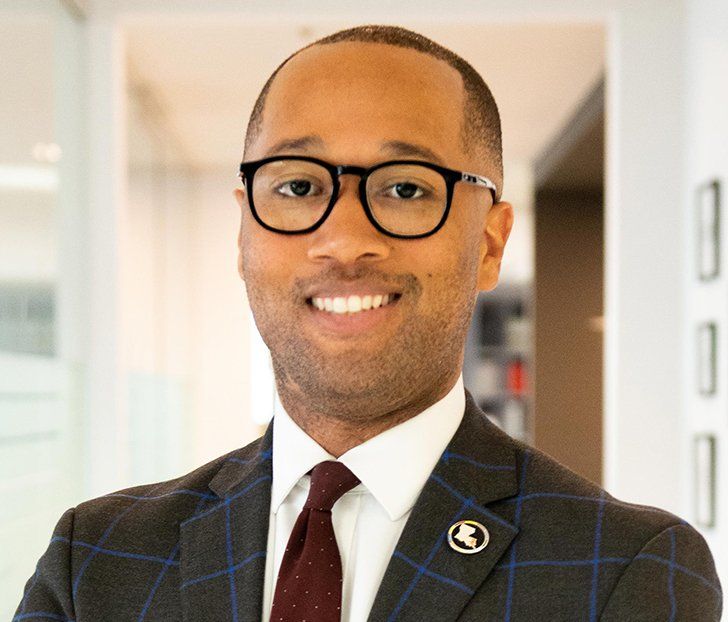 A man wearing glasses and a suit is smiling for the camera