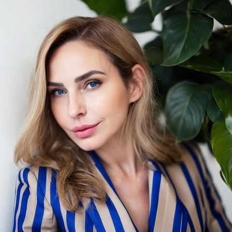 A woman in a striped jacket is leaning against a wall next to a plant.