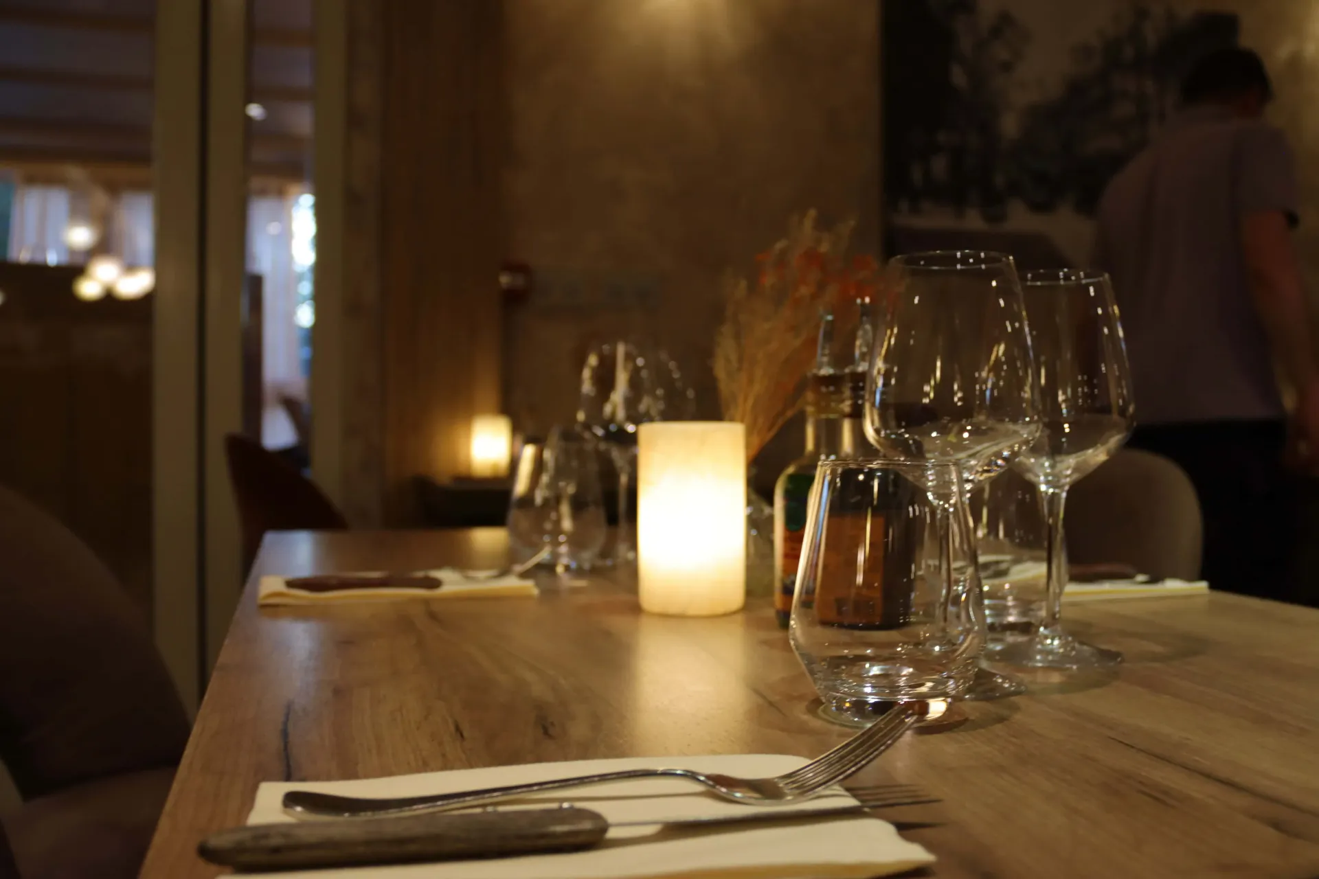 Table de restaurant dressée pour le dîner avec bougie allumée, verres et couverts.