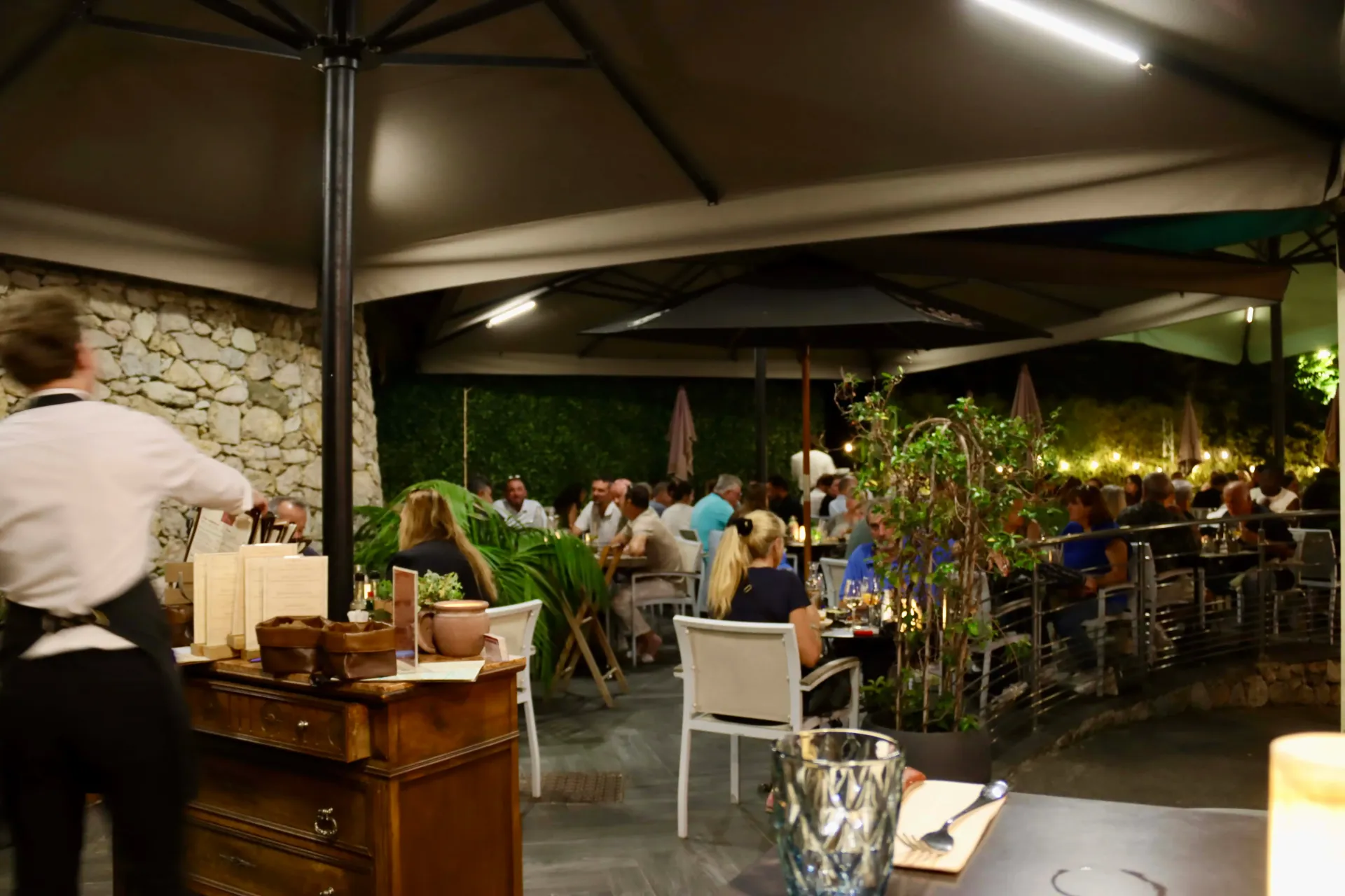 Terrasse de restaurant en plein air la nuit, de nombreuses personnes dînant sous des parasols.