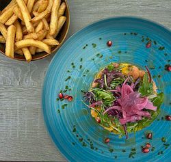Tartare de saumon sur assiette bleue, avec frites en bol. 