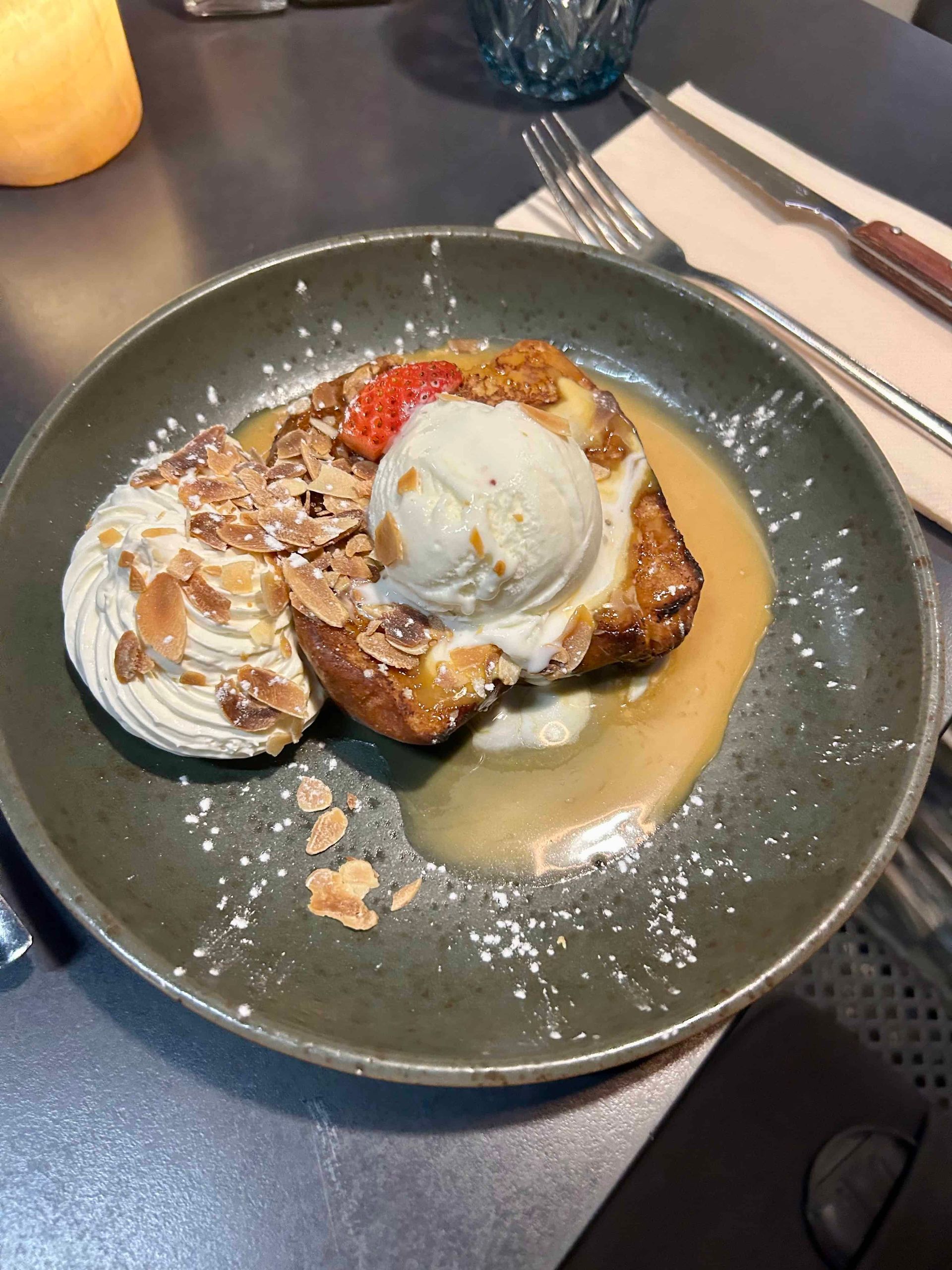 Pain perdu avec glace, crème fouettée, amandes effilées et sauce sur une assiette verte.