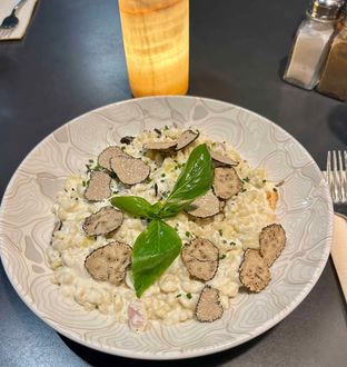 Une assiette de pâtes crémeuses garnie de tranches de truffe fraîche et d'une feuille de basilic, posée sur une table sombre à côté d'une lampe.