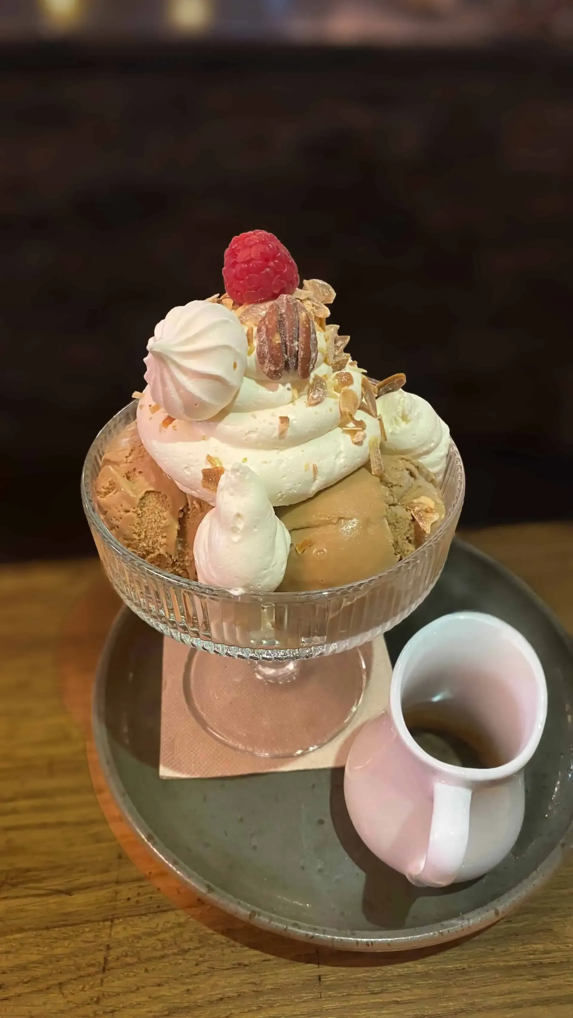Coupe glacée avec crème glacée, crème fouettée, meringue, noix et framboise, servie dans un petit pichet.