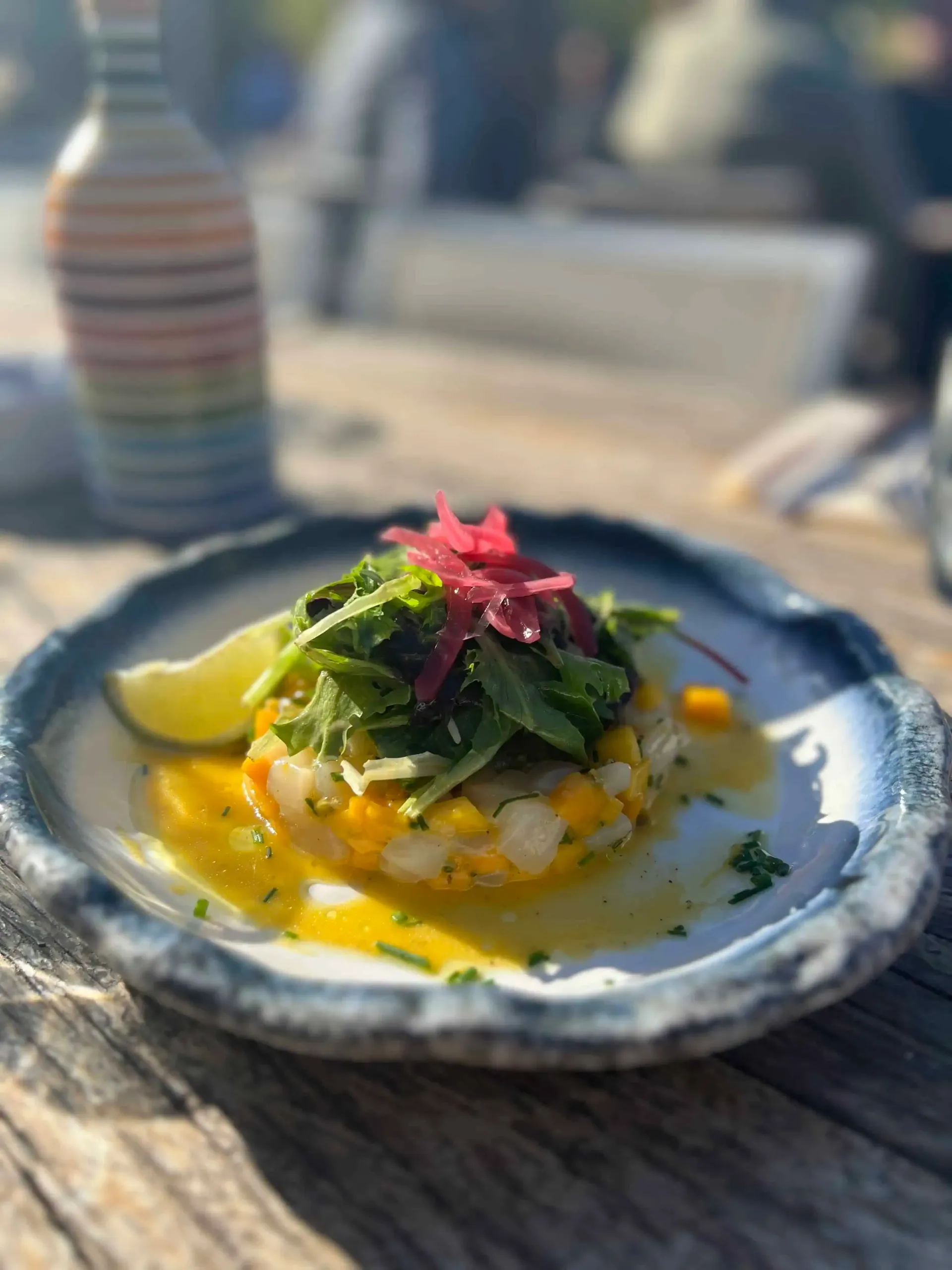 Plat de fruits de mer sur une assiette à bord bleu avec sauce à la mangue, herbes et oignons marinés, cadre extérieur.