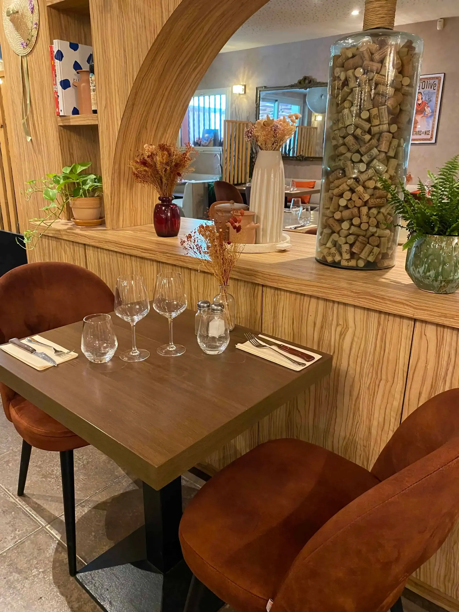 Table de restaurant confortable avec verres, couverts, deux chaises rouille, un bocal en liège et des fleurs séchées.