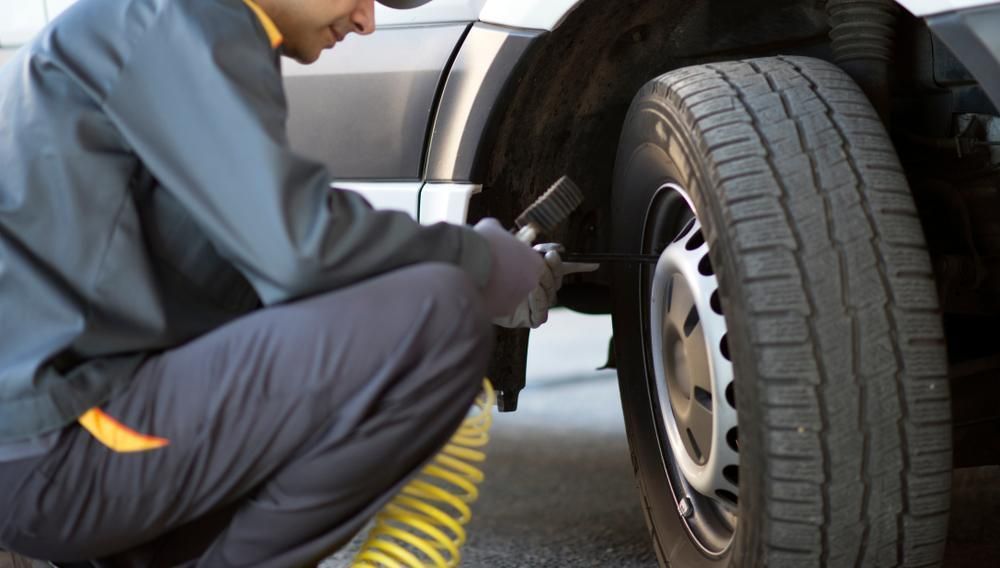 A Man Is Kneeling Down To Change A Tire On A Truck — Summit Smash Toongabbie In Toongabbie, NSW