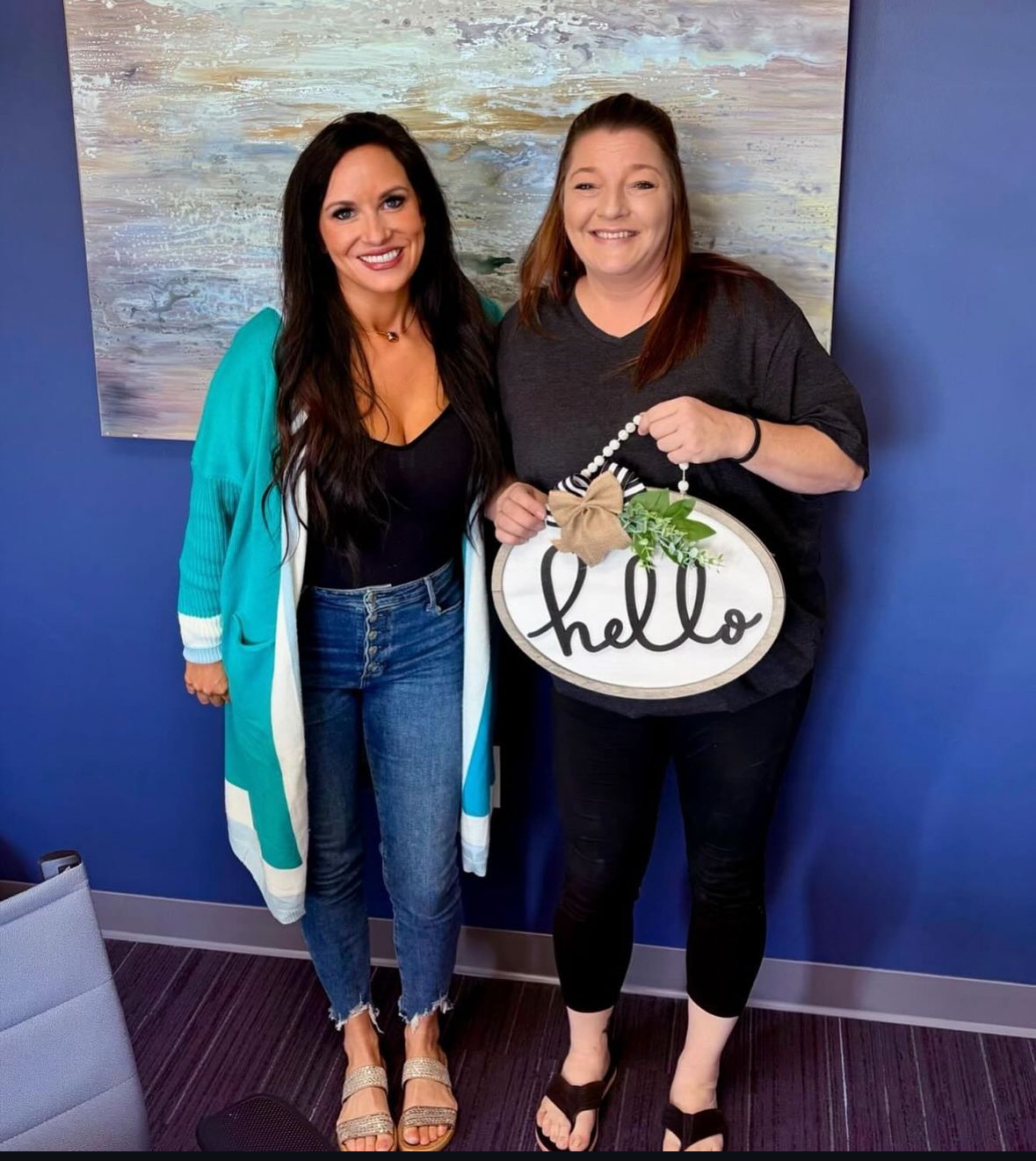 Two women are standing next to each other holding a hello sign.
