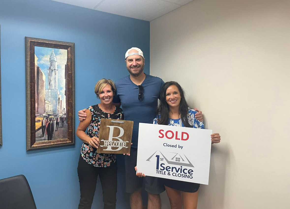 A man and two women are holding a sold sign in a room.