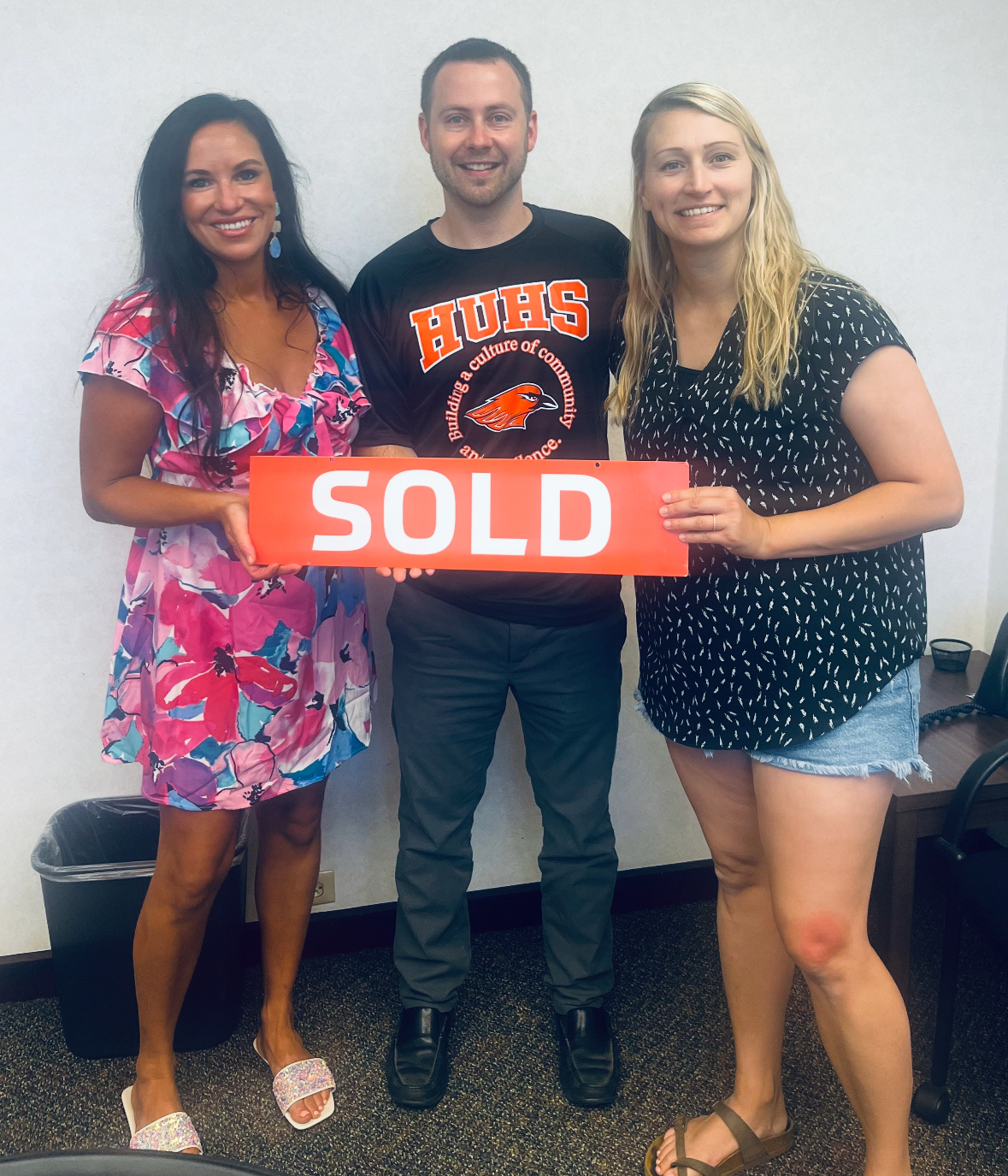 A group of people holding a sign that says sold