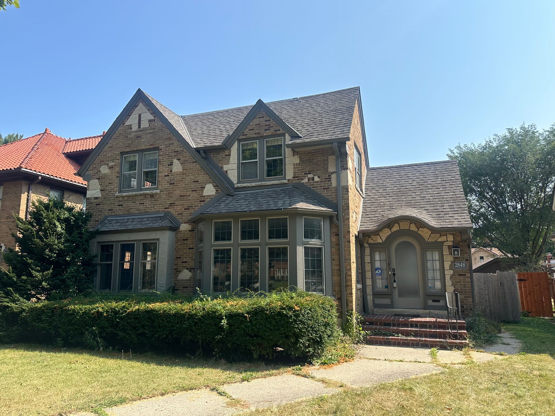A large brick house with a gray roof is sitting on top of a lush green lawn.