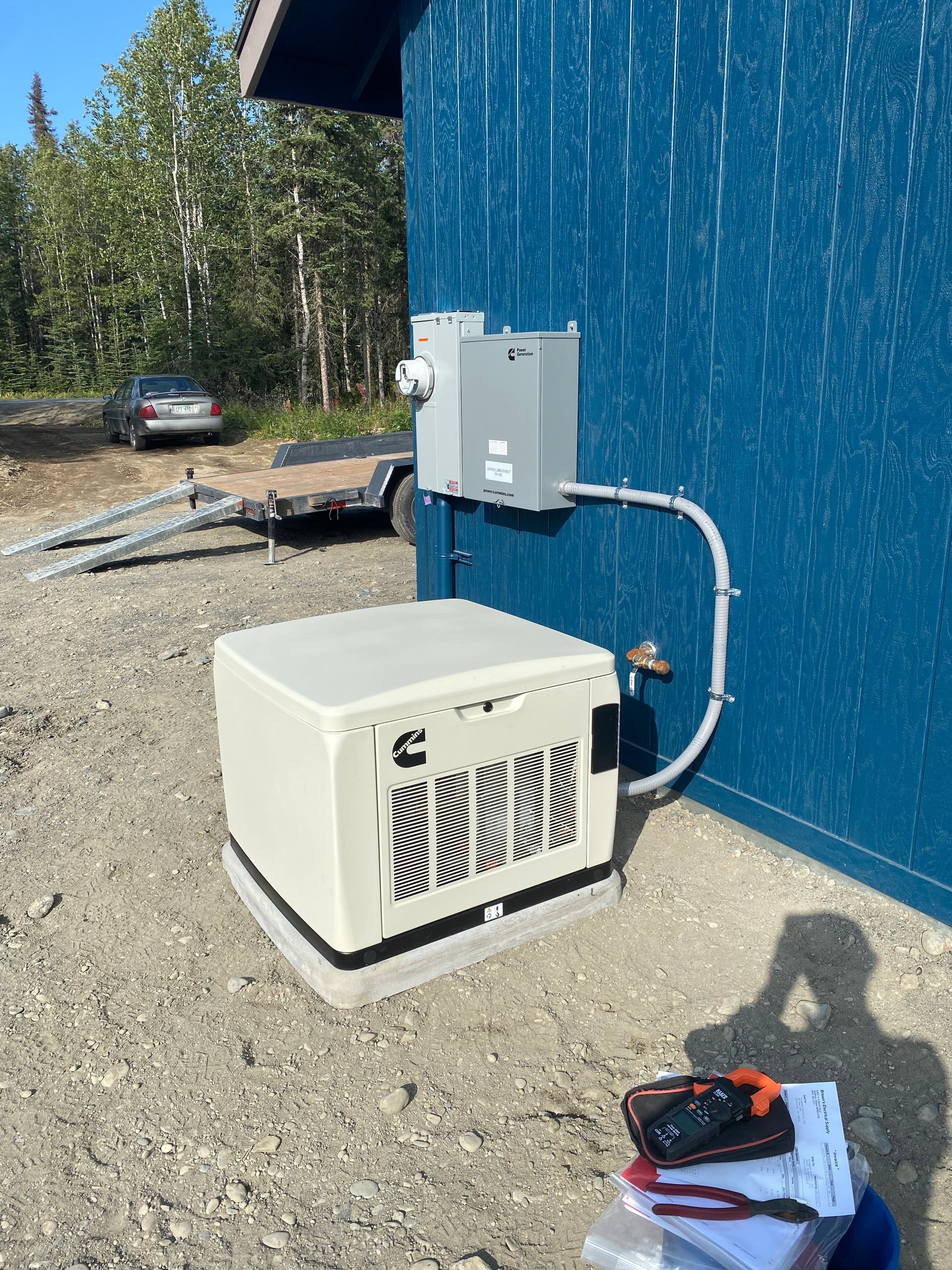 A gray and teal Cummins P4600iDF portable generator with black wheels, in front of a business sign.