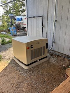 Beige Cummins generator outside a white building on gravel.