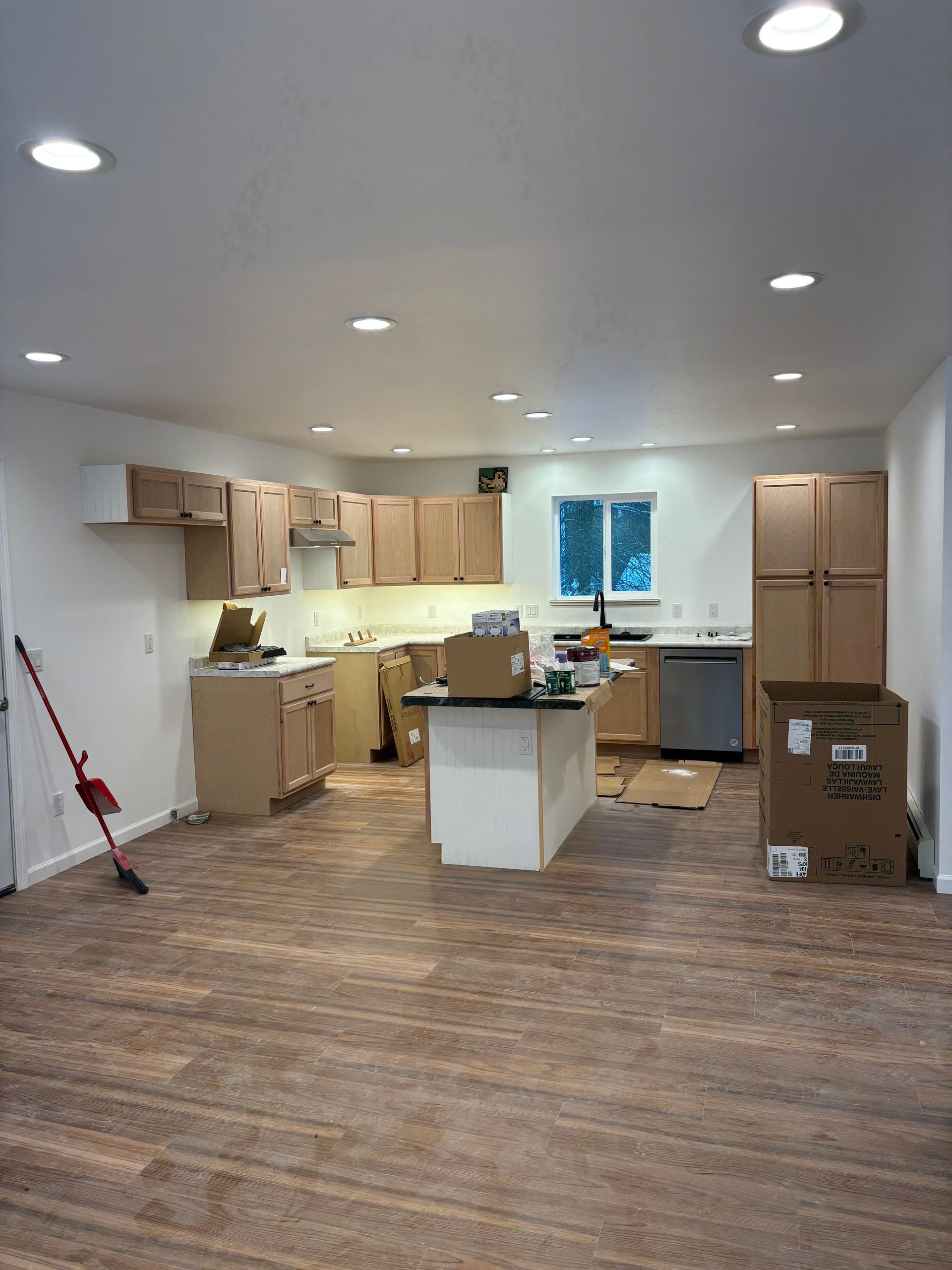 Kitchen with unfinished cabinets, an island, and new flooring; boxes are present.
