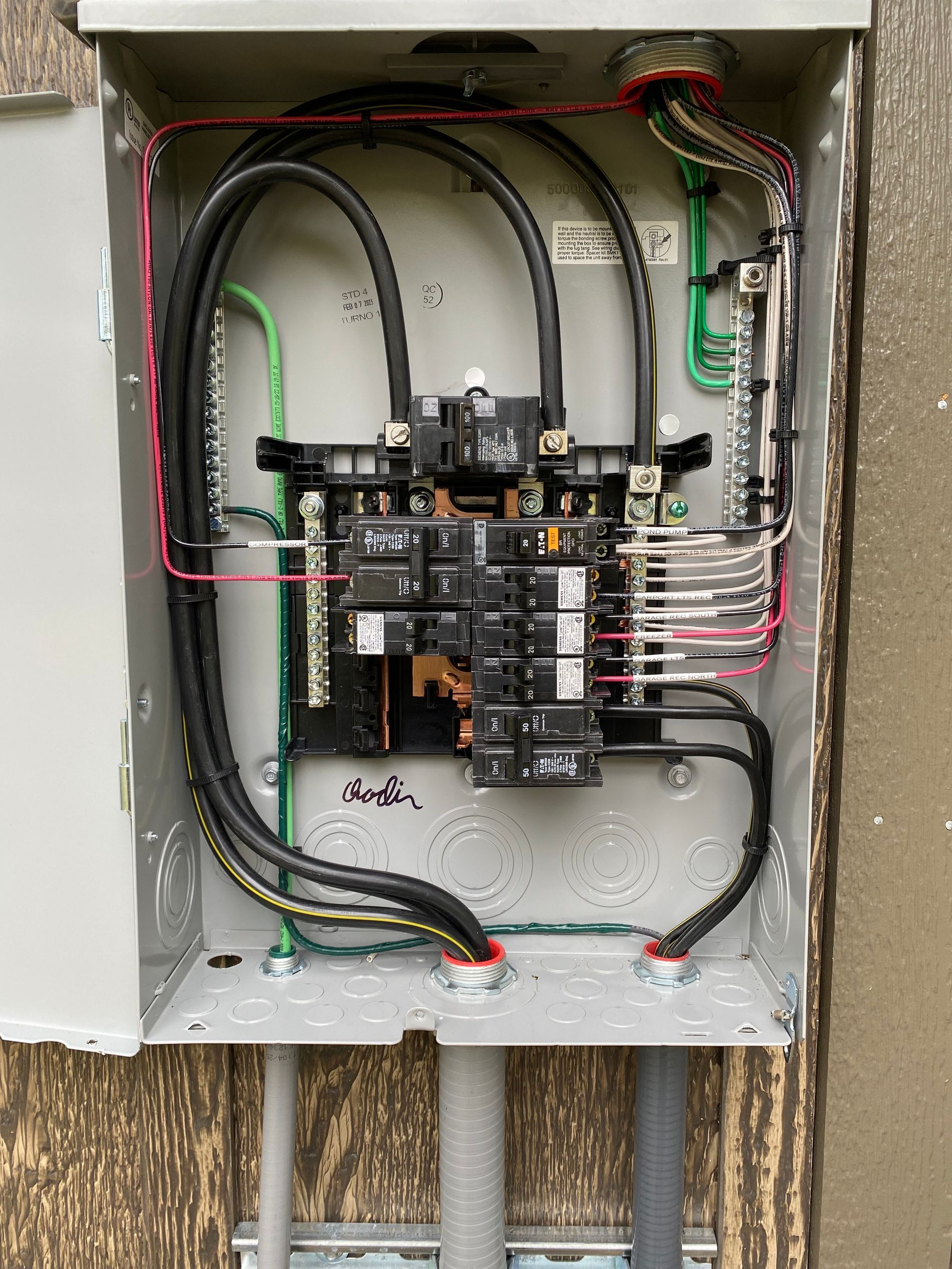 Electrical panel with black and gray wires, green ground wires, and breakers inside a gray metal box.