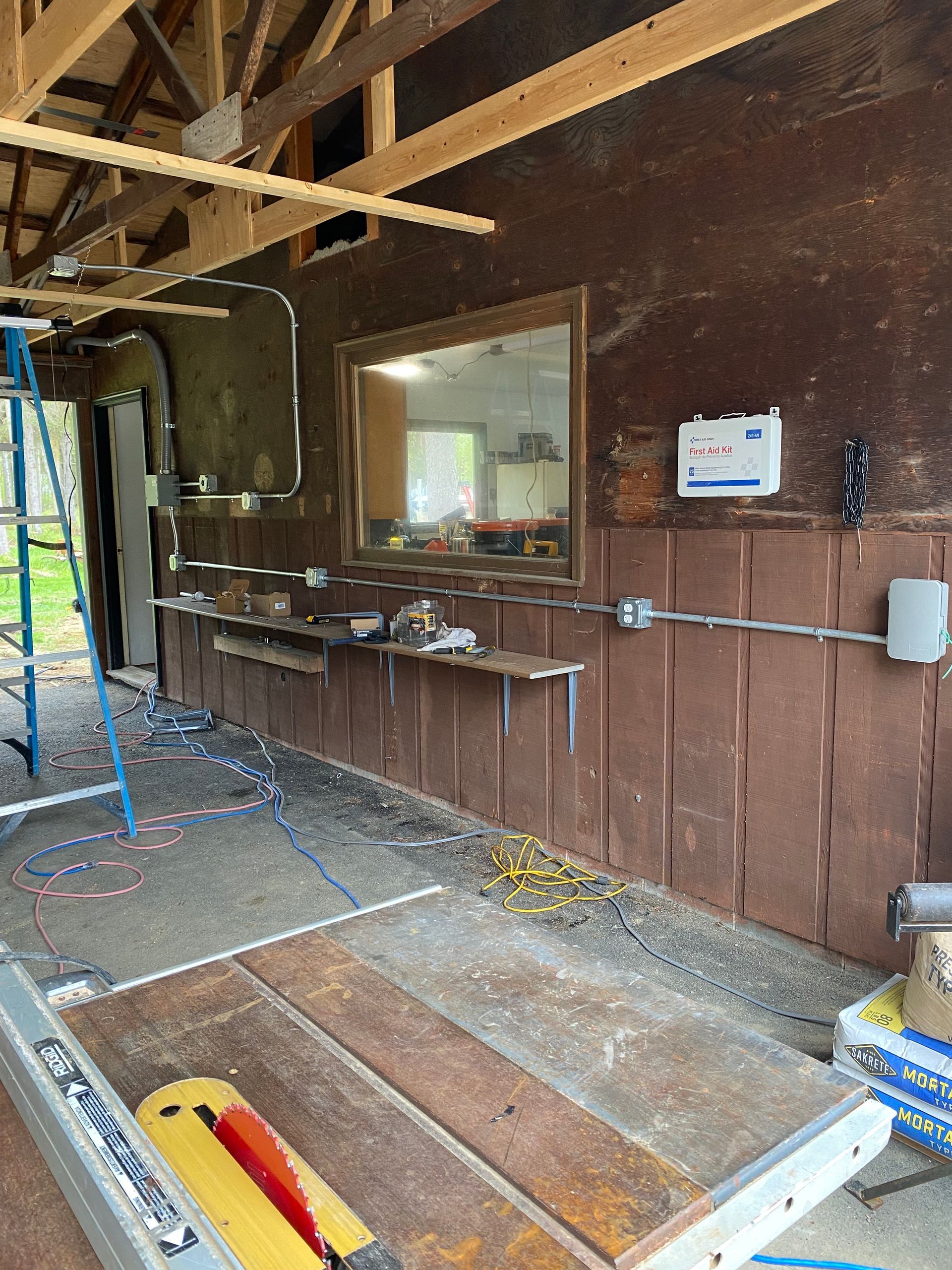 Workshop interior with a table saw, brown walls, a mirror, and exposed wiring.