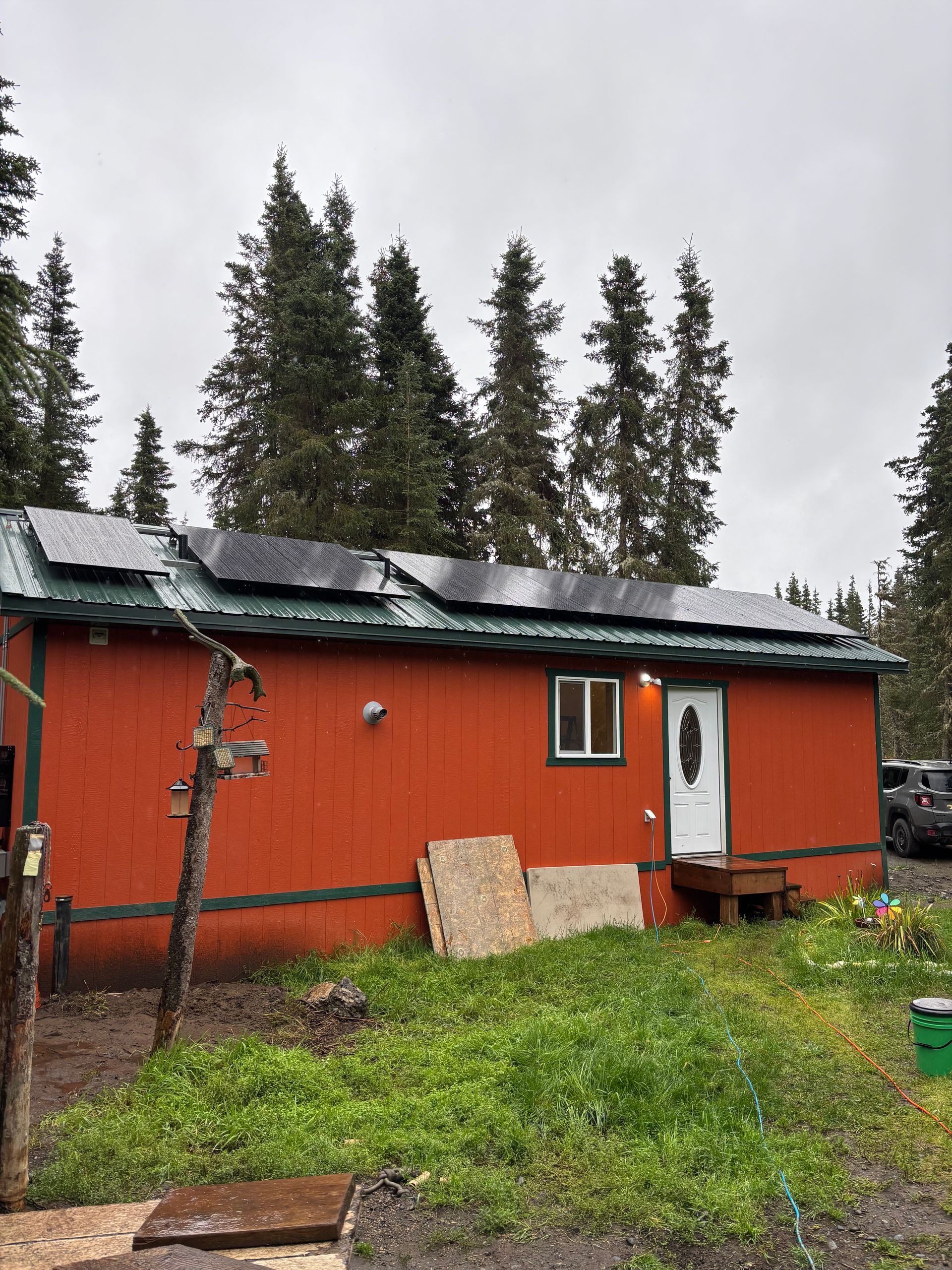 Orange cabin with solar panels on the roof, surrounded by trees and overgrown grass.