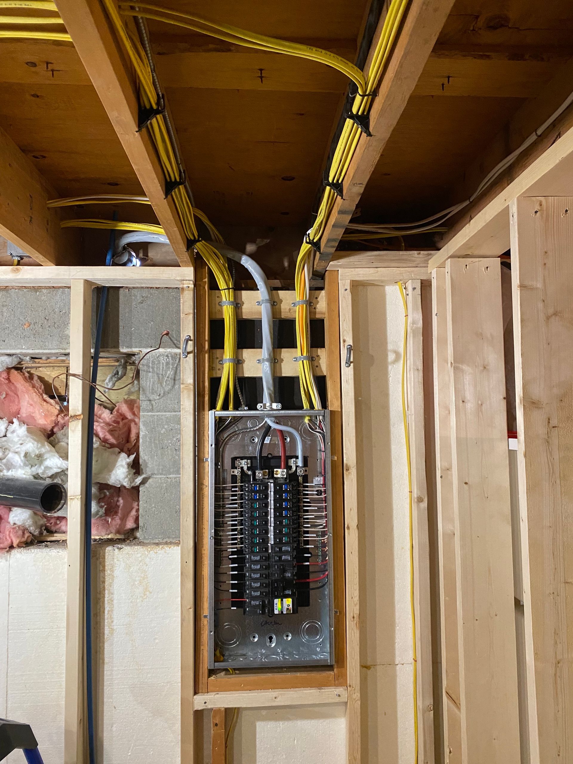 Electrical panel in a wooden frame, with yellow wires running overhead. Wires secured by black clips.