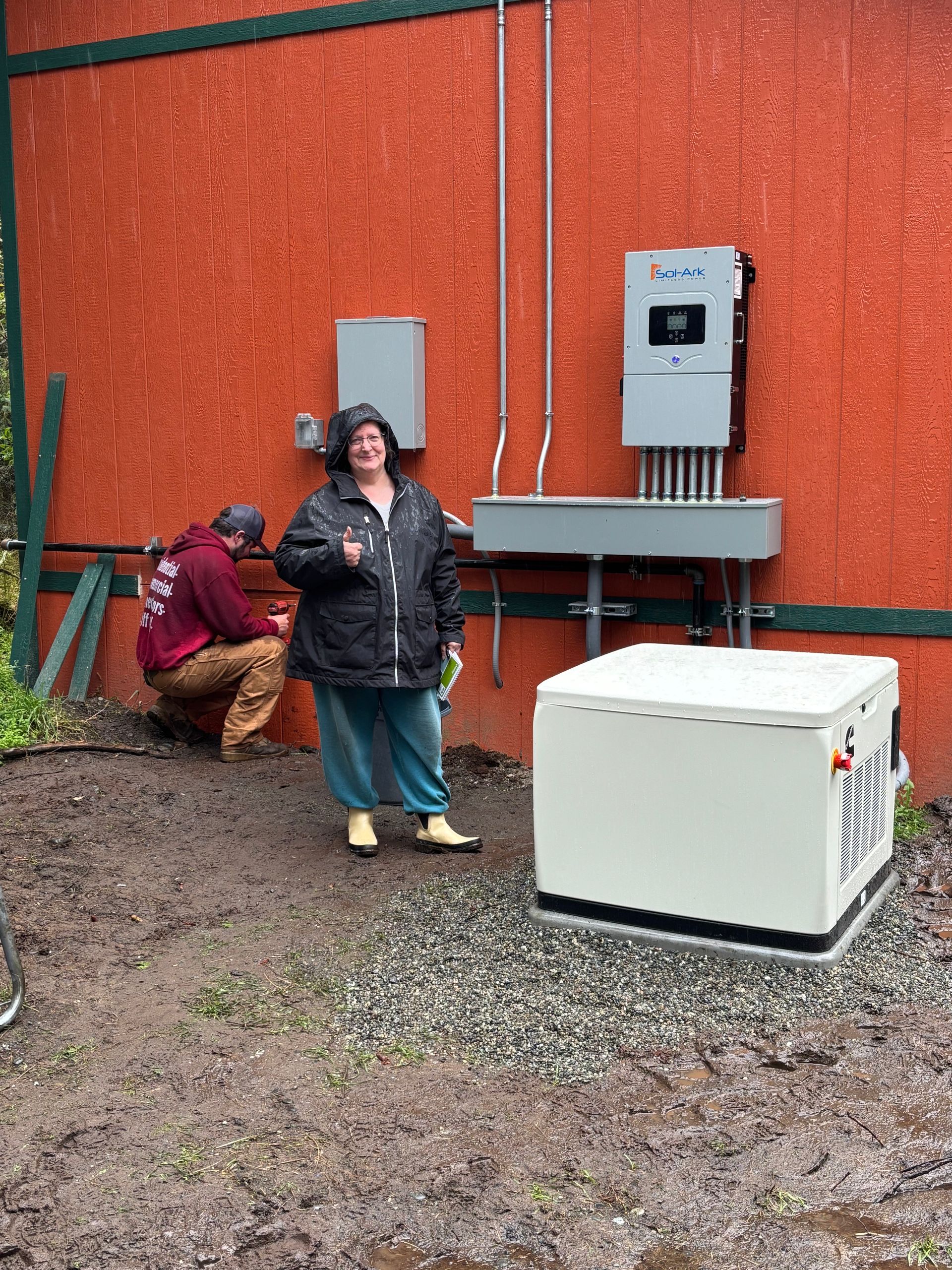 Woman stands near solar panel equipment while another man works outside a building.