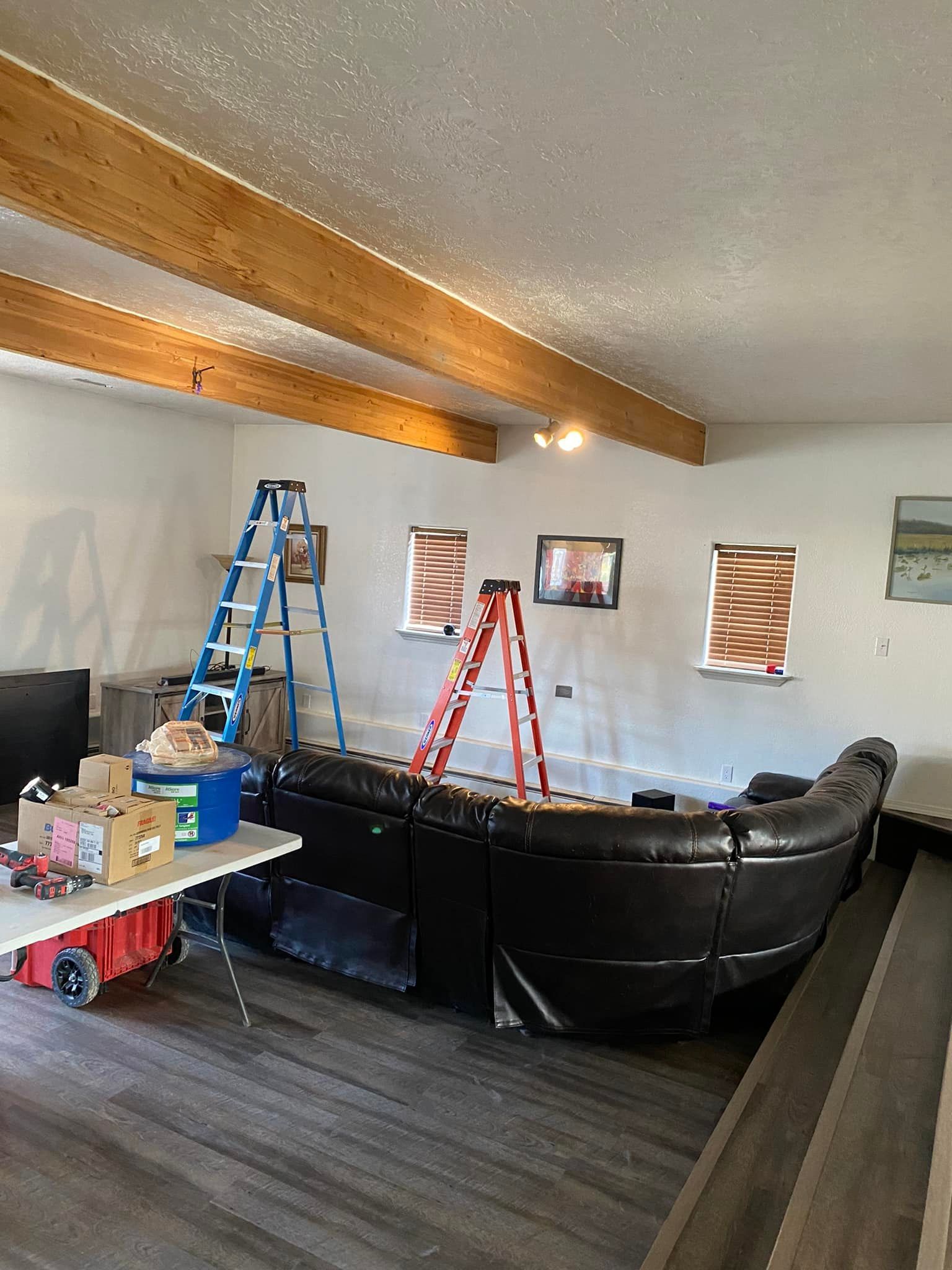 Interior with sectional sofa, ladders, artwork on wall, wooden beams.
