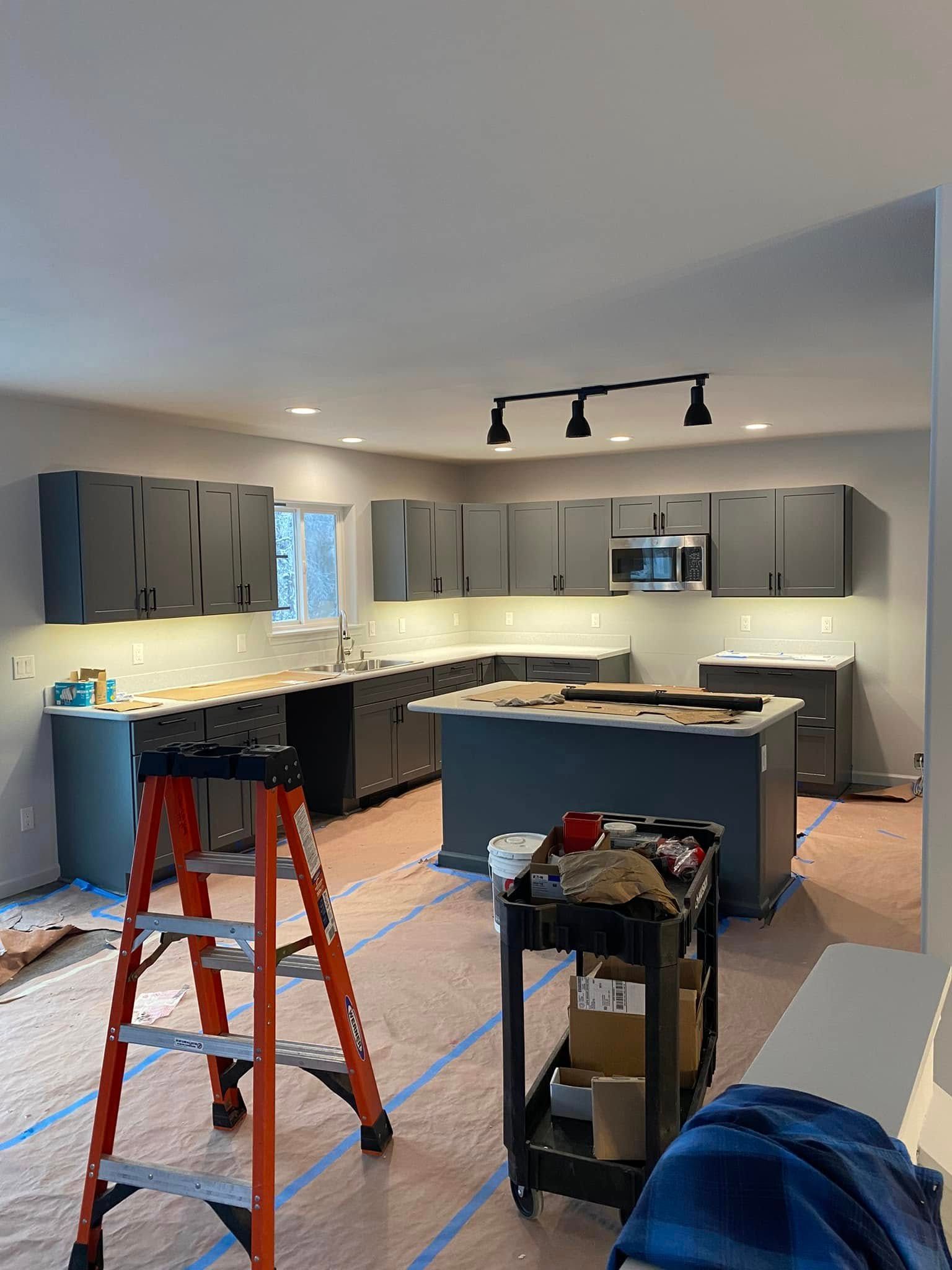 Kitchen remodel in progress with gray cabinets and island, tools, and a ladder.