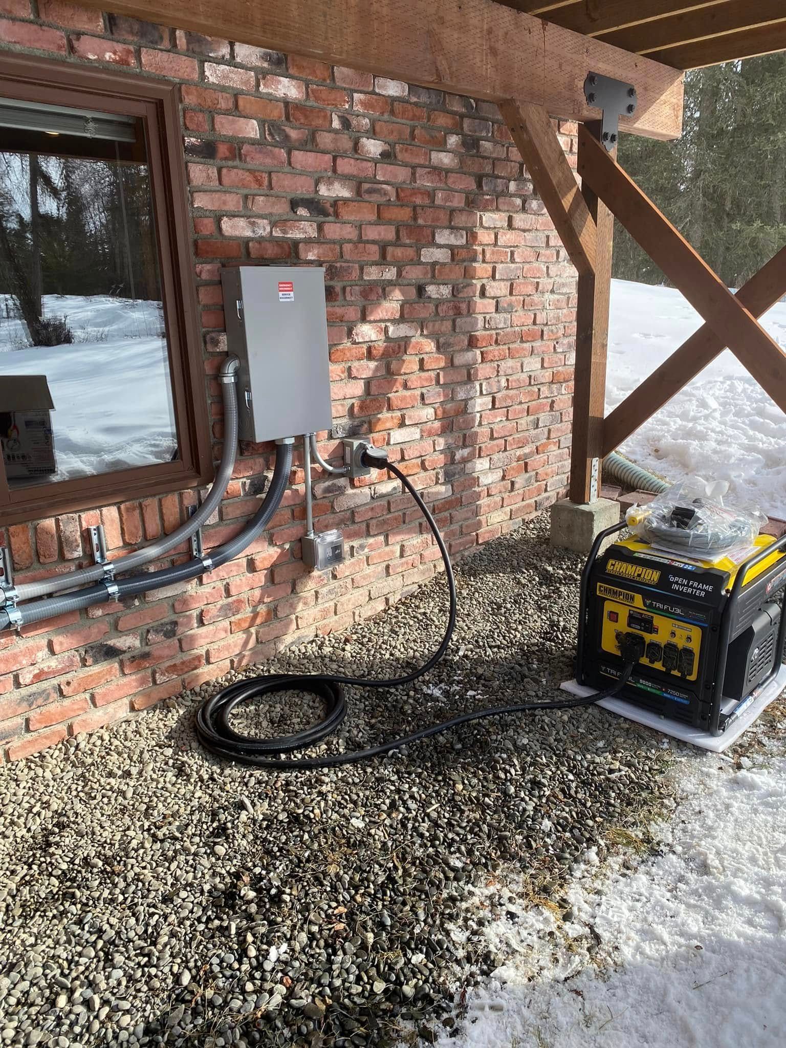Generator connected to a power panel on a brick building with snow and gravel.