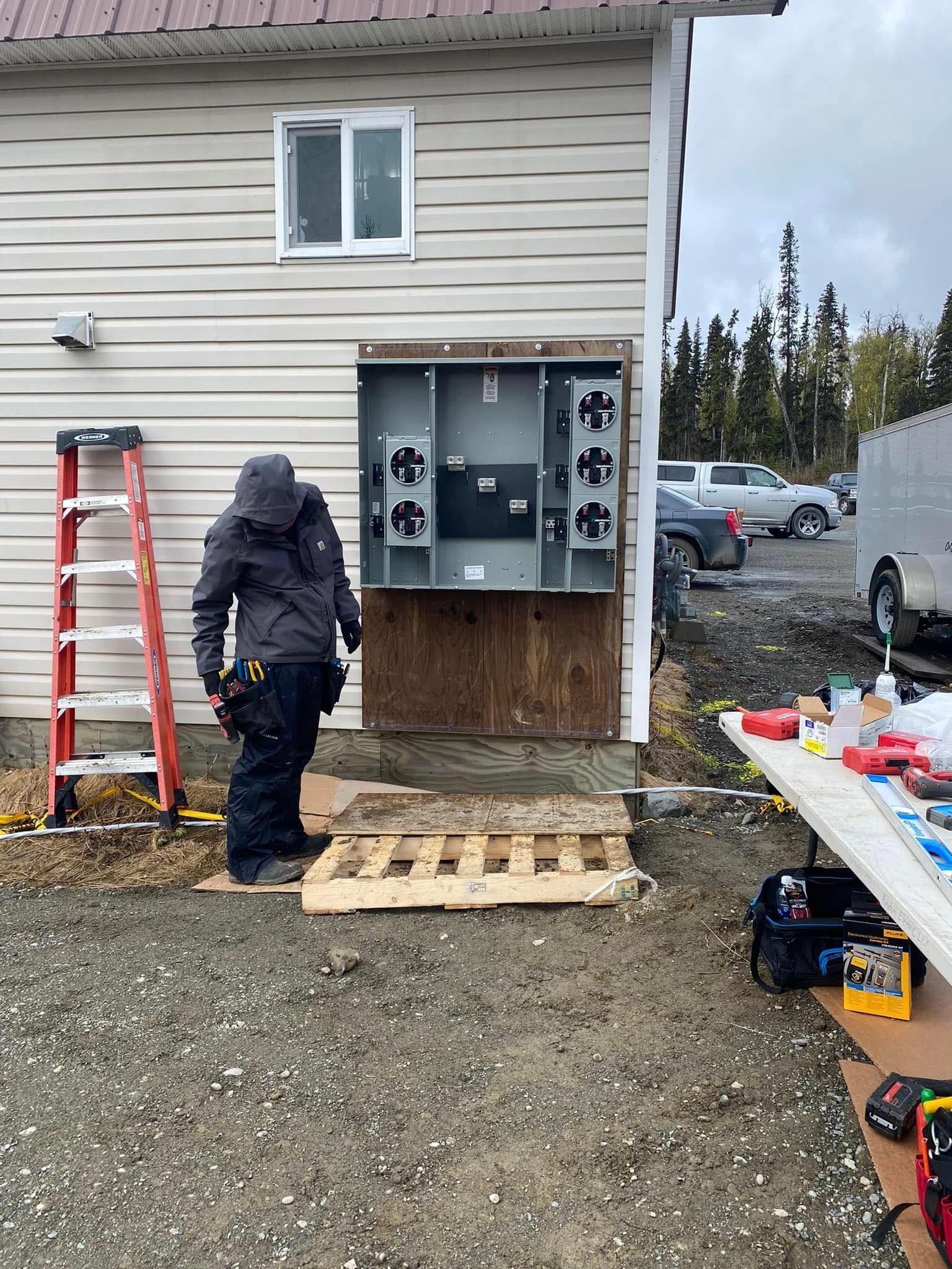 Electrician working on electrical panel on the side of a building. Outdoor construction site.