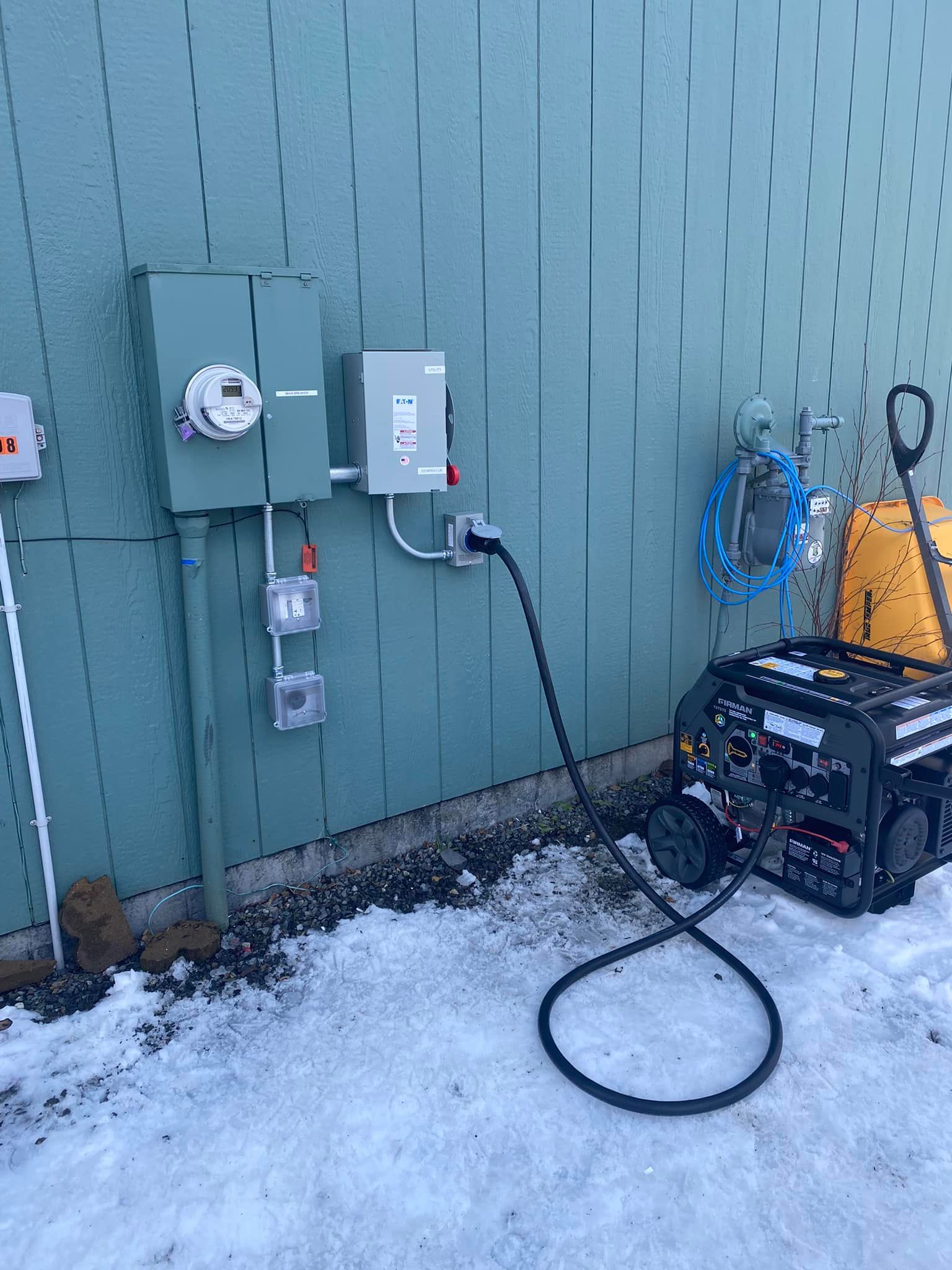 Generator connected to a house's electrical panel on a snow-covered ground.