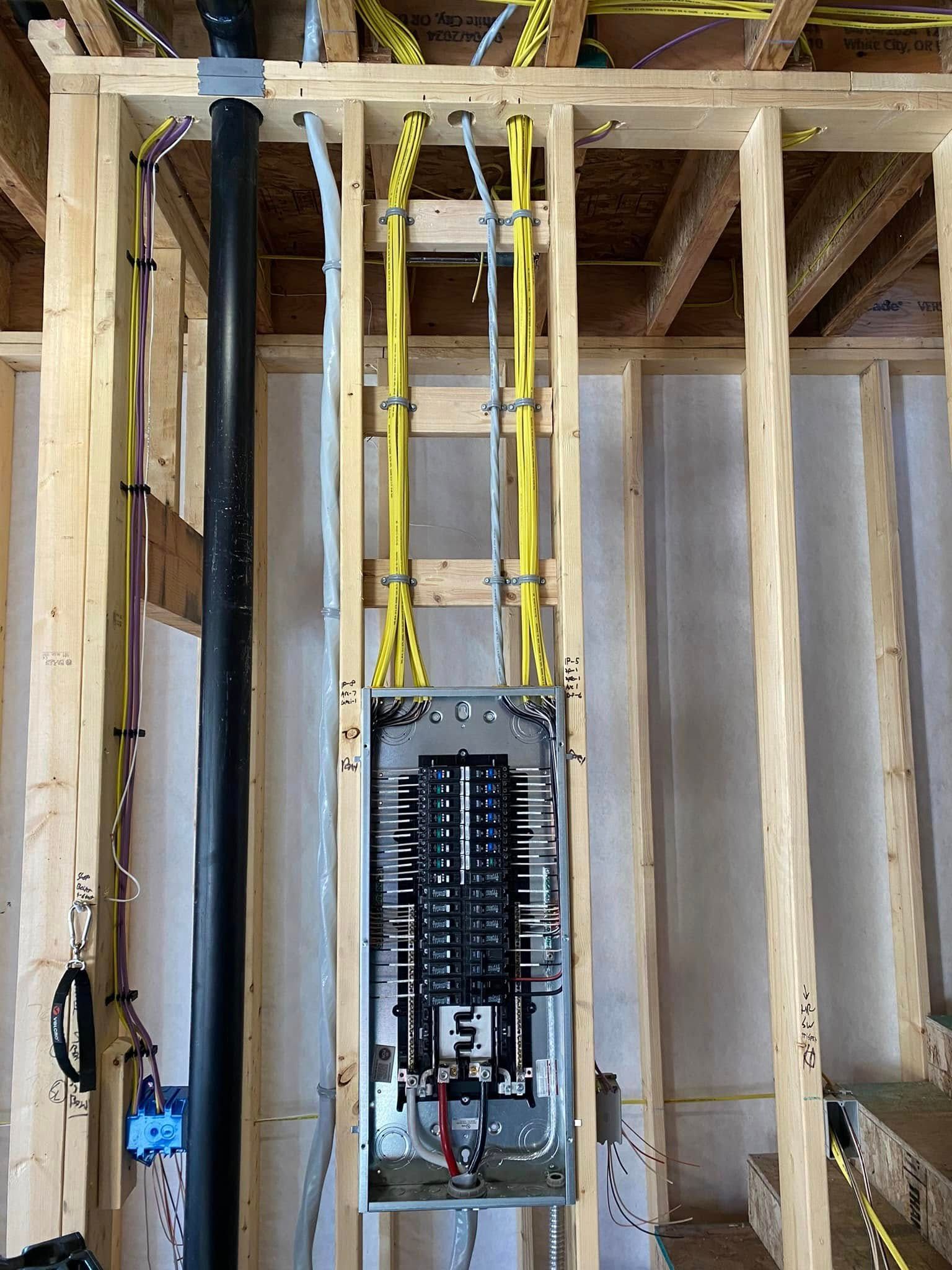 Electrical panel installed in wooden framing; black conduit, yellow wires.