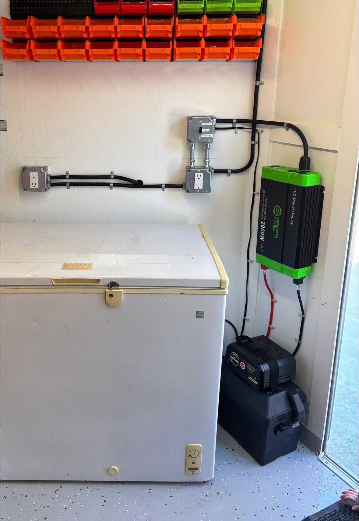White freezer, battery, and green inverter hooked up to electrical outlets.