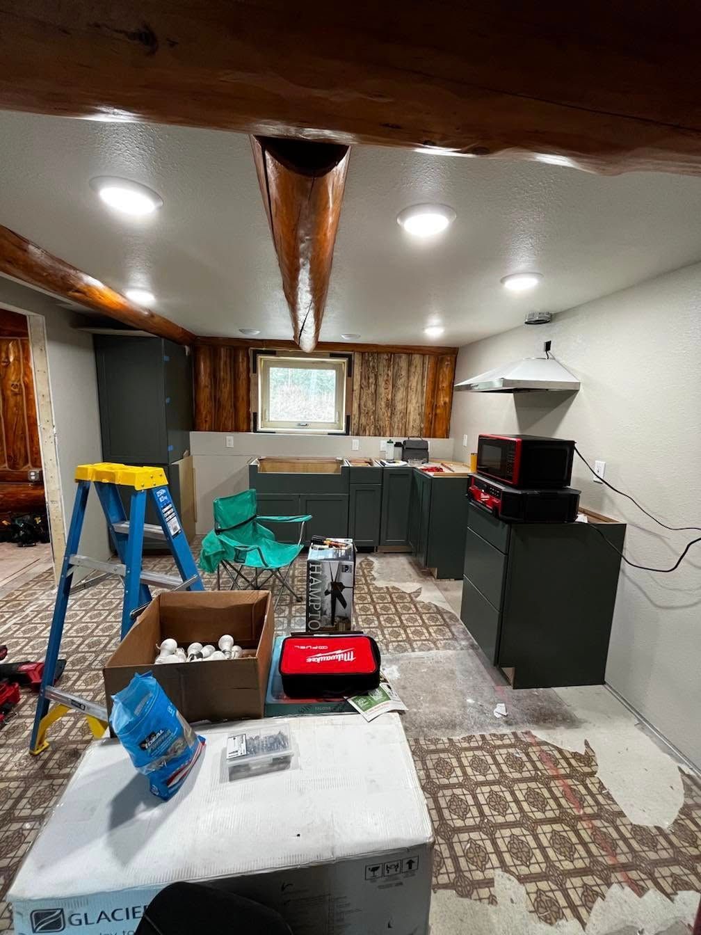 Kitchen renovation in progress. Green cabinets, exposed wood accents, tools, and boxes scattered on the floor.