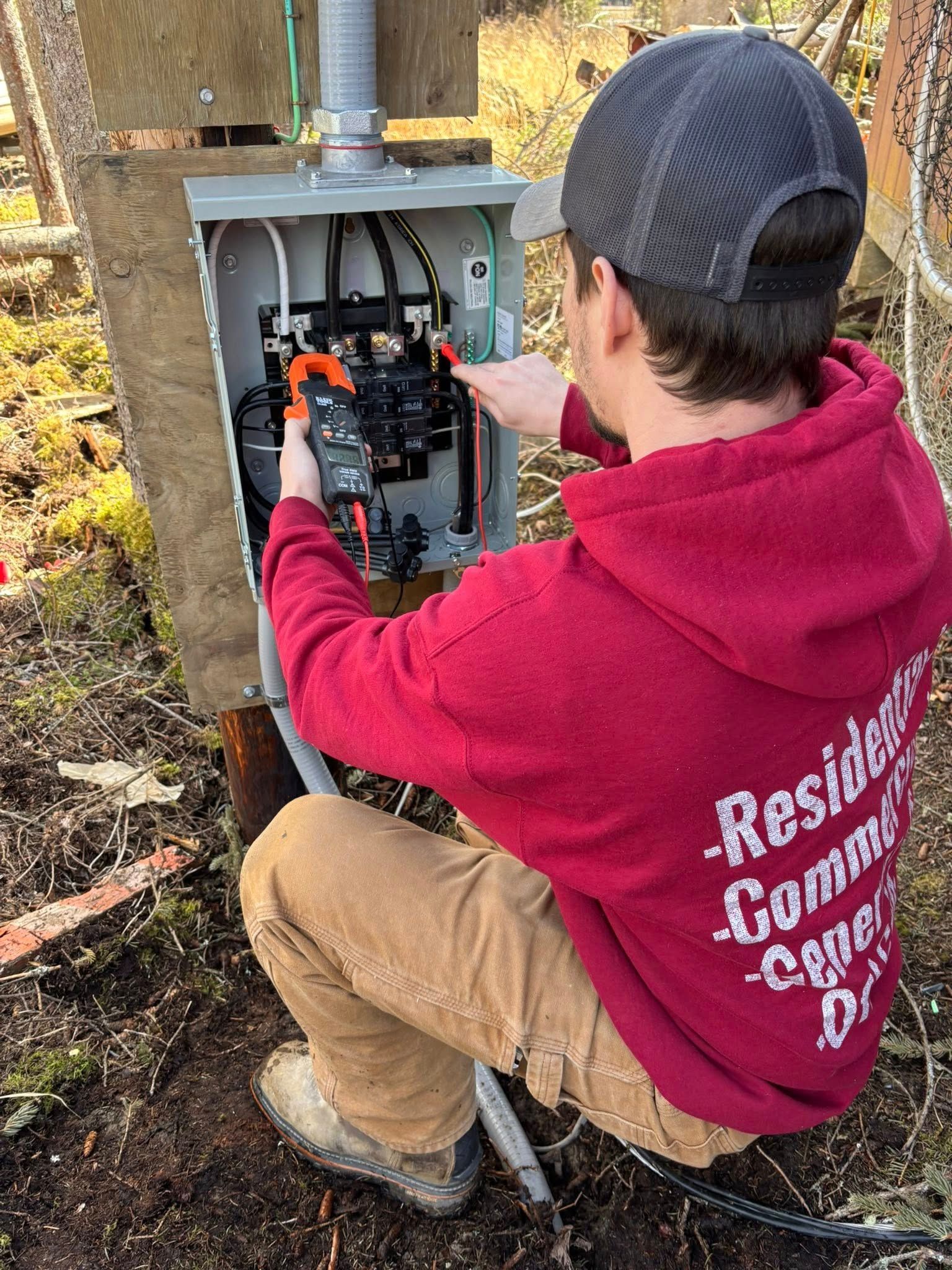 Electrician in red hoodie working on electrical box outdoors.