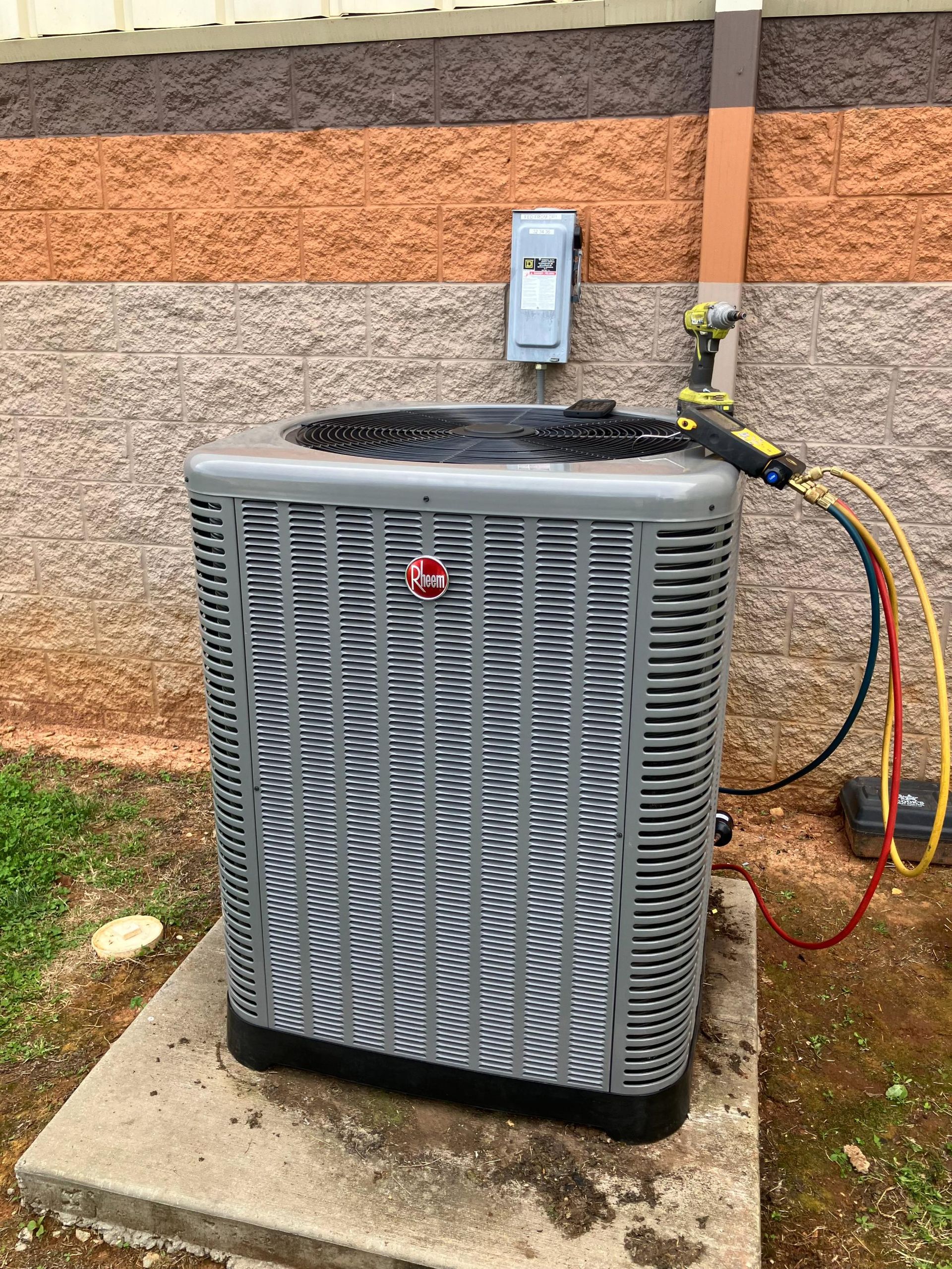 A gray air conditioner is sitting on a concrete platform next to a brick wall.