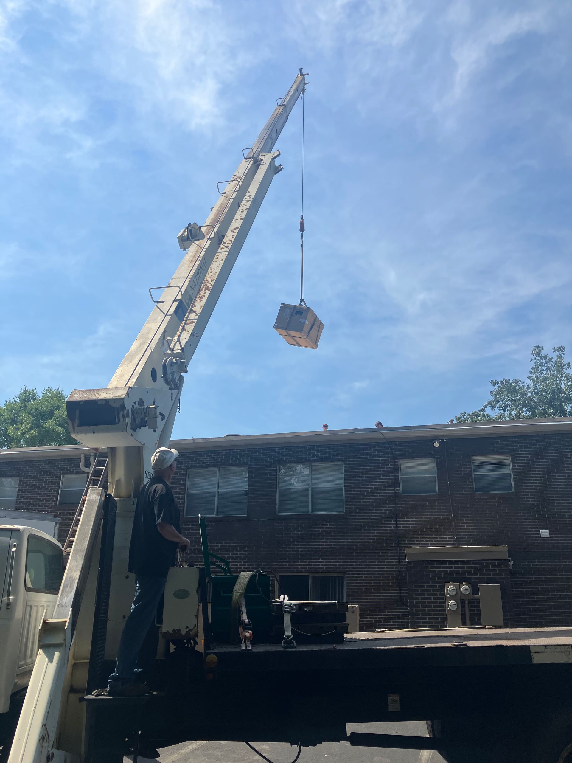 A crane is lifting a box from a truck in front of a log cabin.
